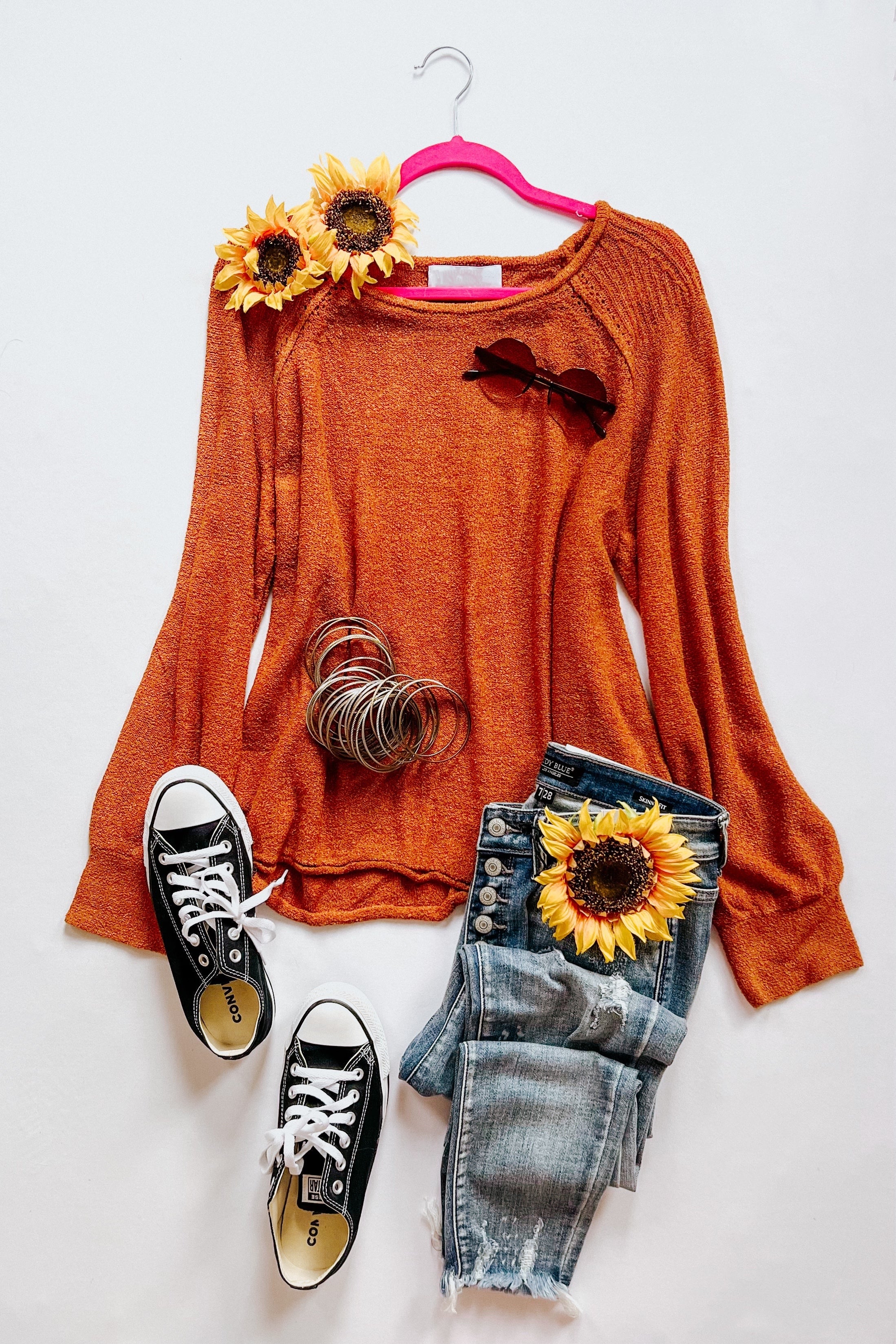 Rust-colored knit pullover sweater with flared sleeves paired with distressed blue jeans and black canvas sneakers laid out flat