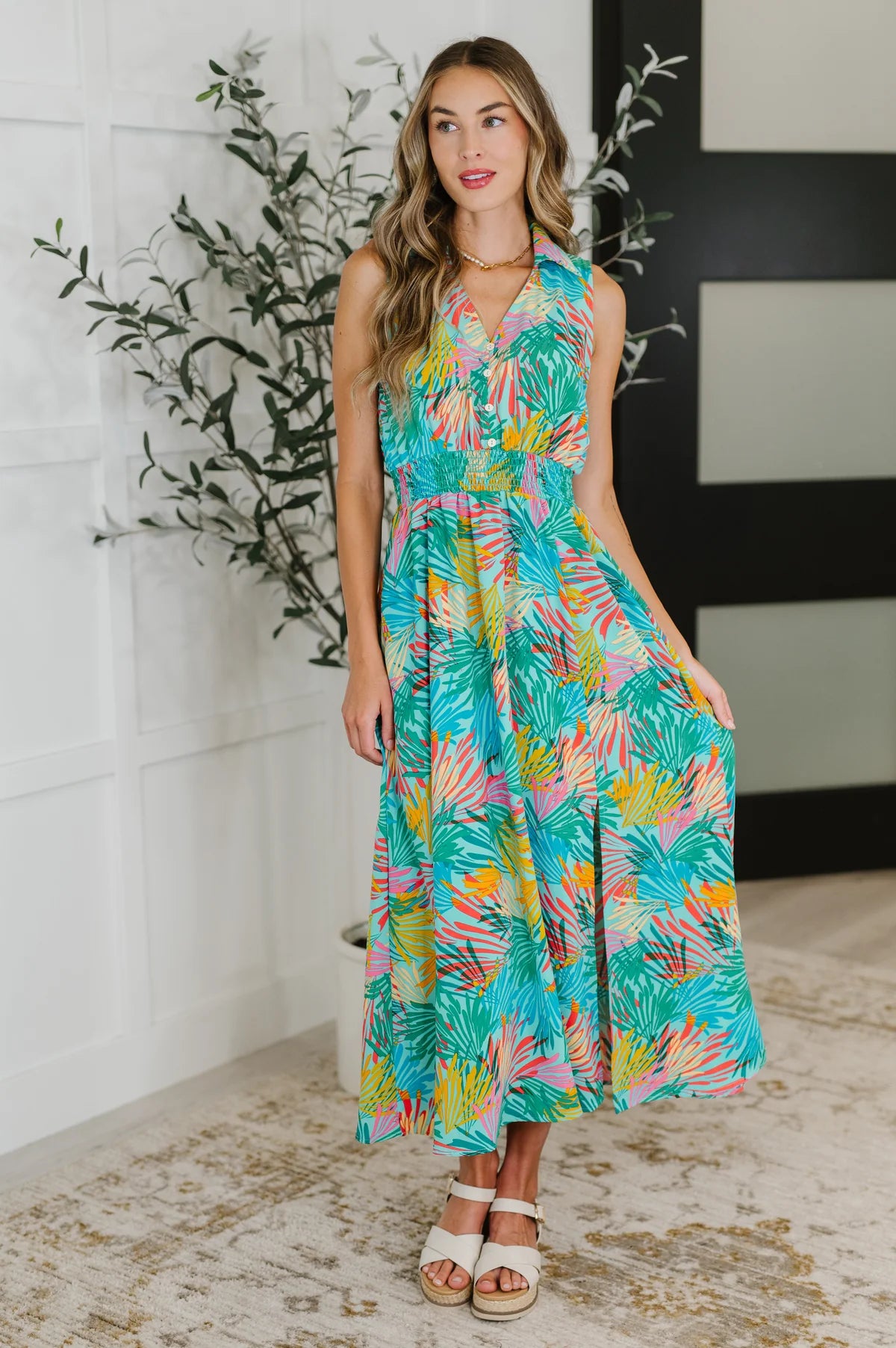 Woman wearing sleeveless tropical print maxi dress with collared neckline and smocked waist posing indoors