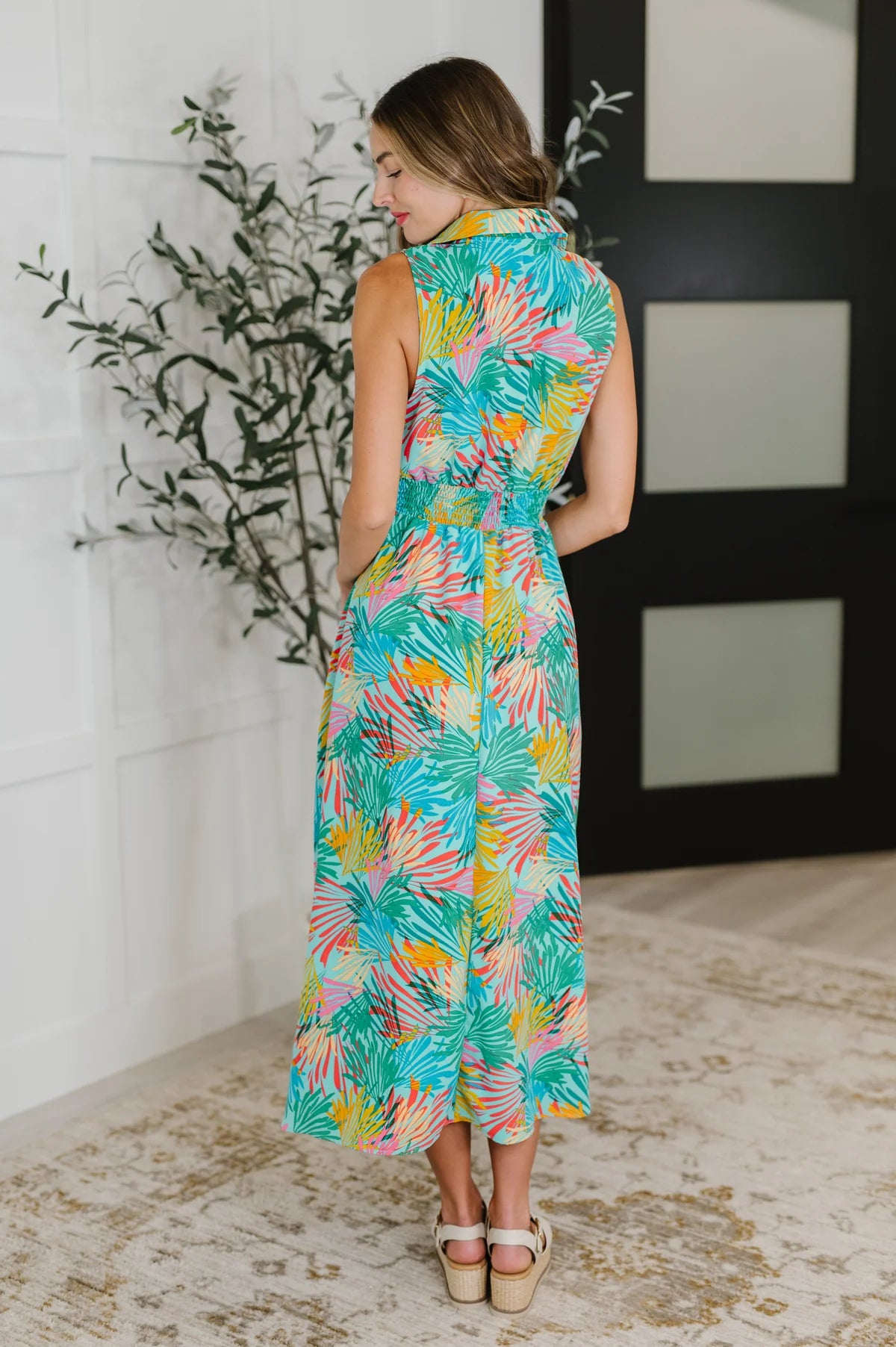 Woman wearing sleeveless tropical print midi dress with collar standing indoors with hands in pockets