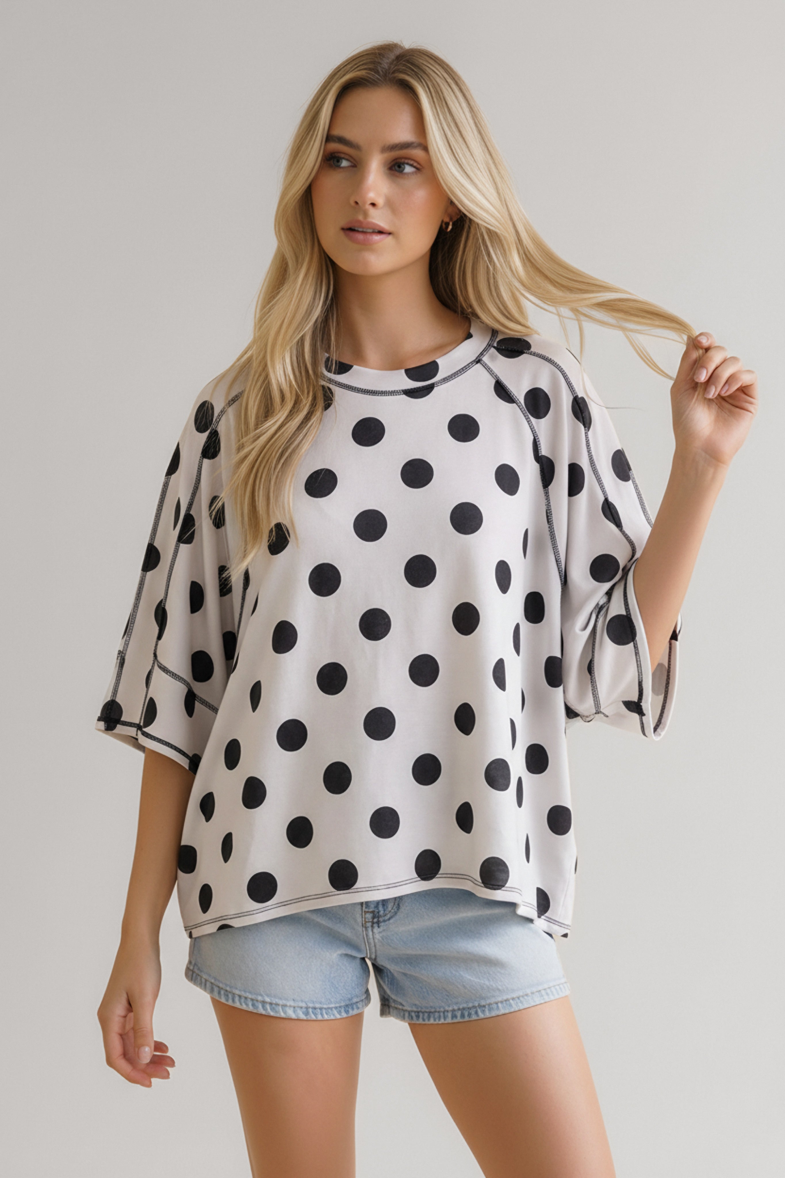 Woman wearing loose black and white polka dot top with wide sleeves paired with light denim shorts in casual look