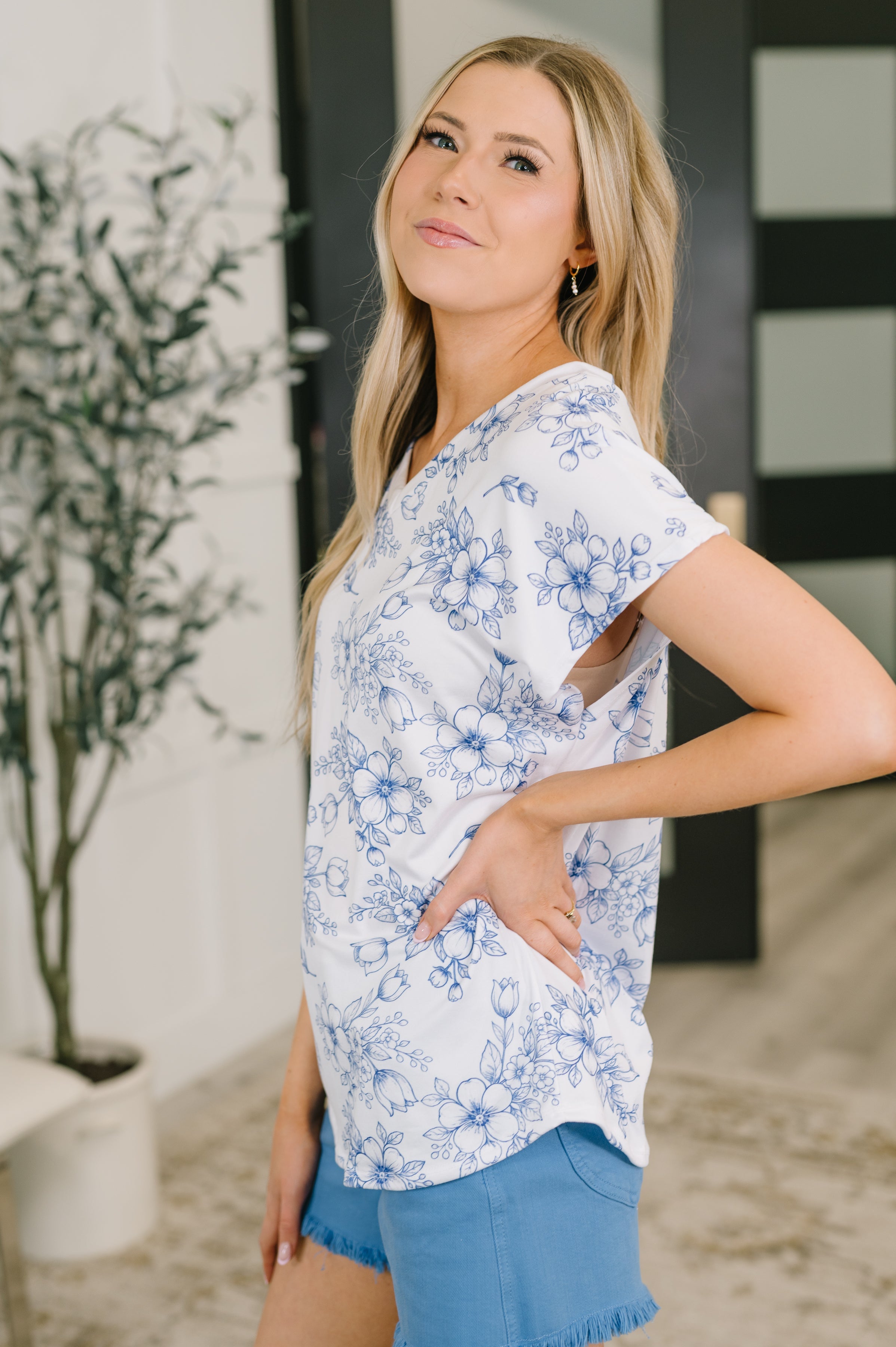 Woman wearing a cream V-neck top with delicate blue floral print paired with casual blue denim shorts indoors