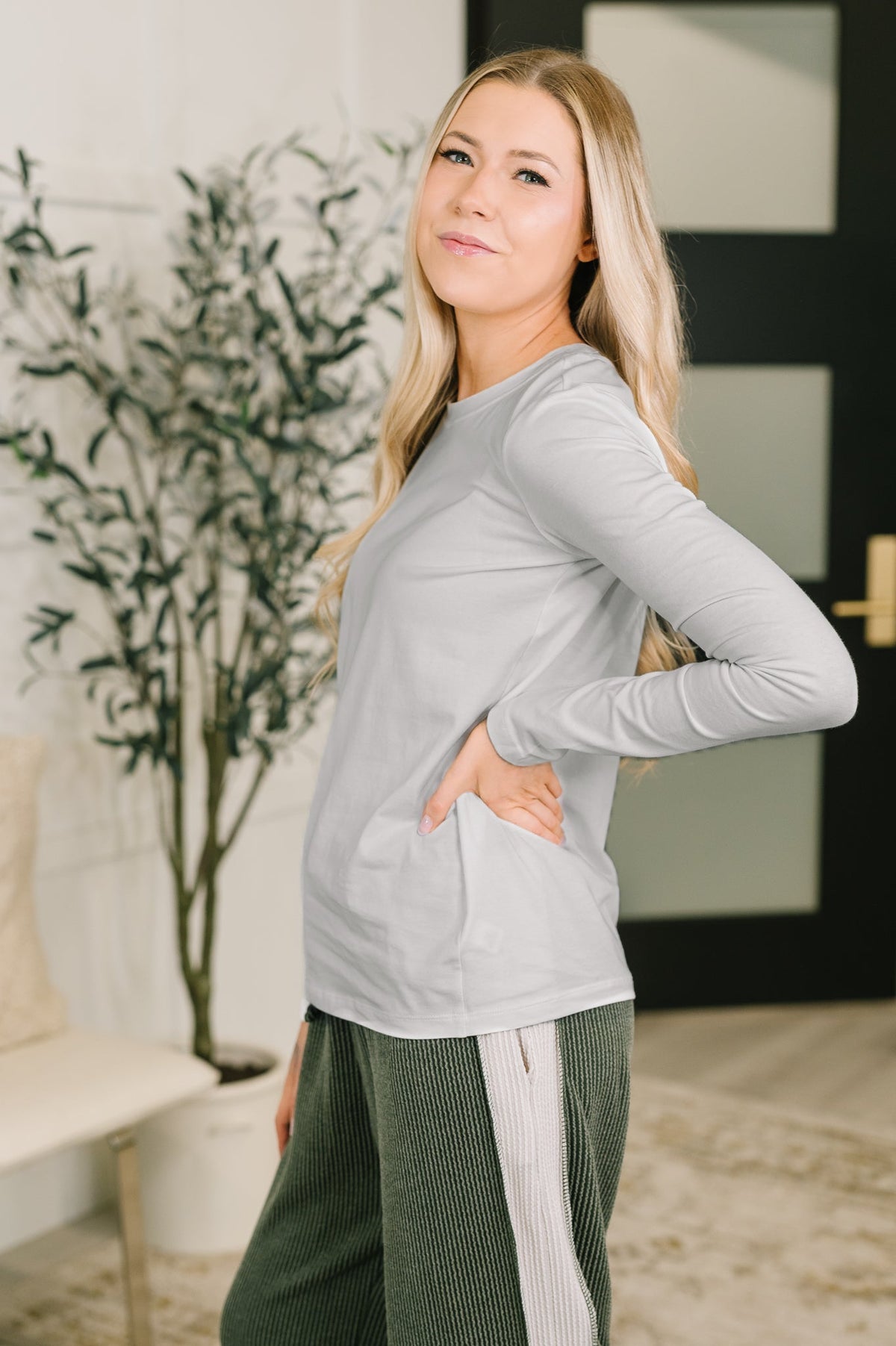 Smiling woman wearing a soft grey long sleeve top with green striped pants in a modern home interior