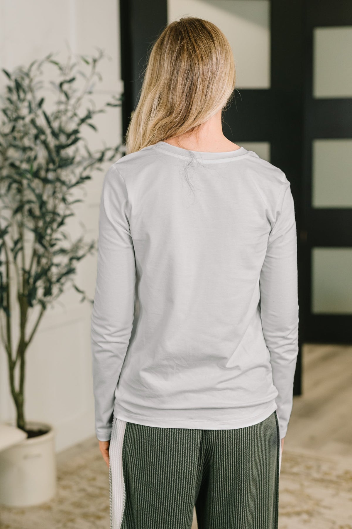 Back view of a woman wearing a heathered grey long sleeve top with ribbed dark trousers in a contemporary home