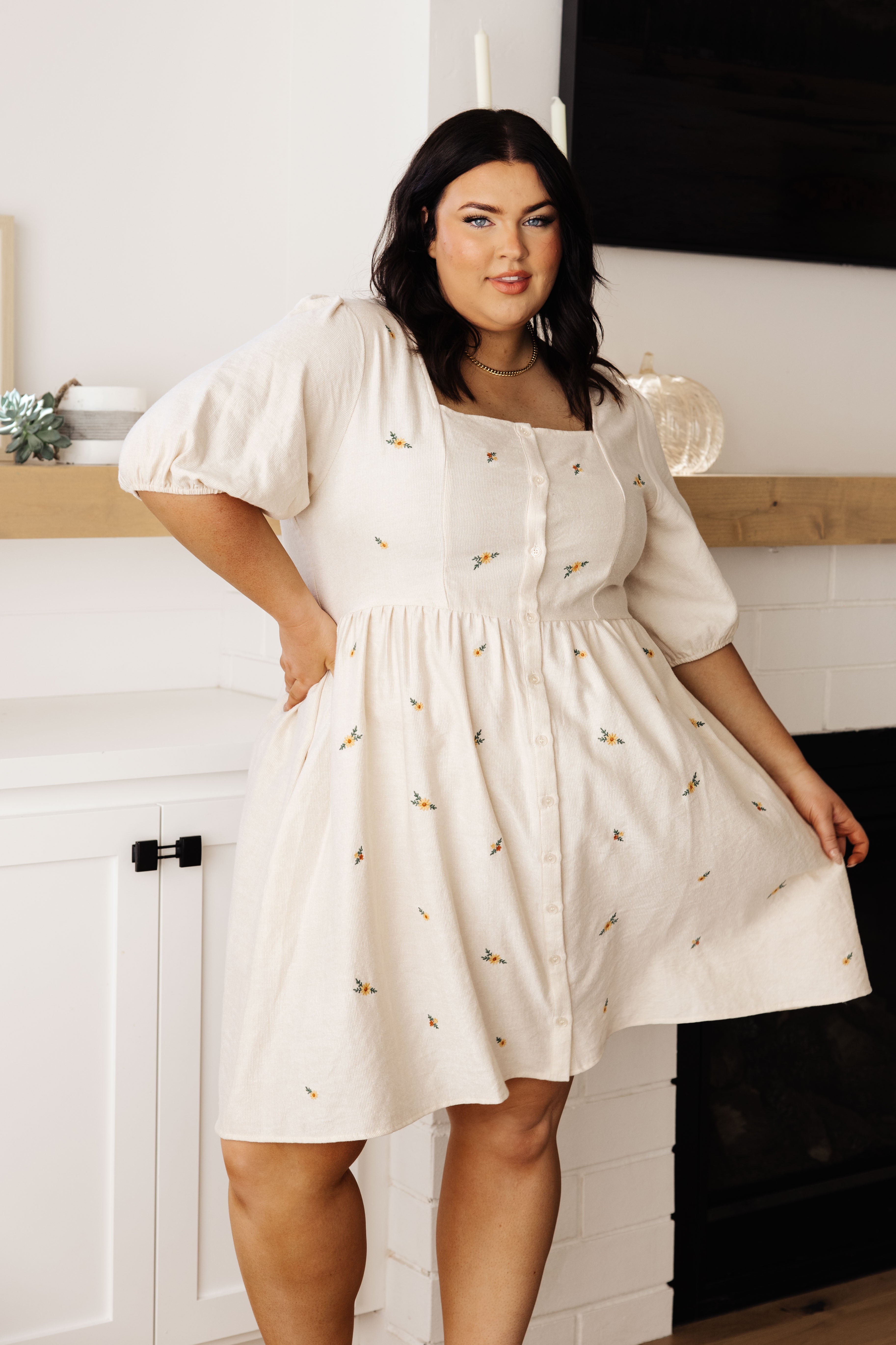 Plus size model indoors wearing cream dress with puff sleeves, square neckline, button front, and small floral embroidery