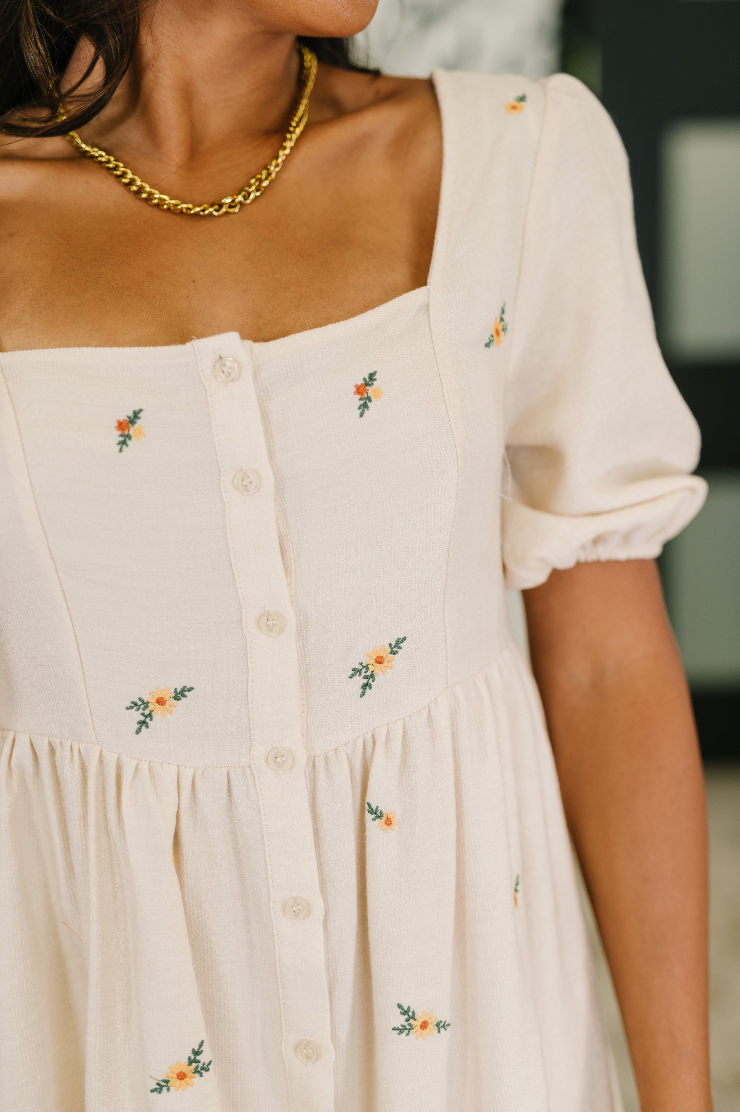 Close-up of cream-colored dress with small orange floral embroidery, puff sleeves, square neckline, and button-down front