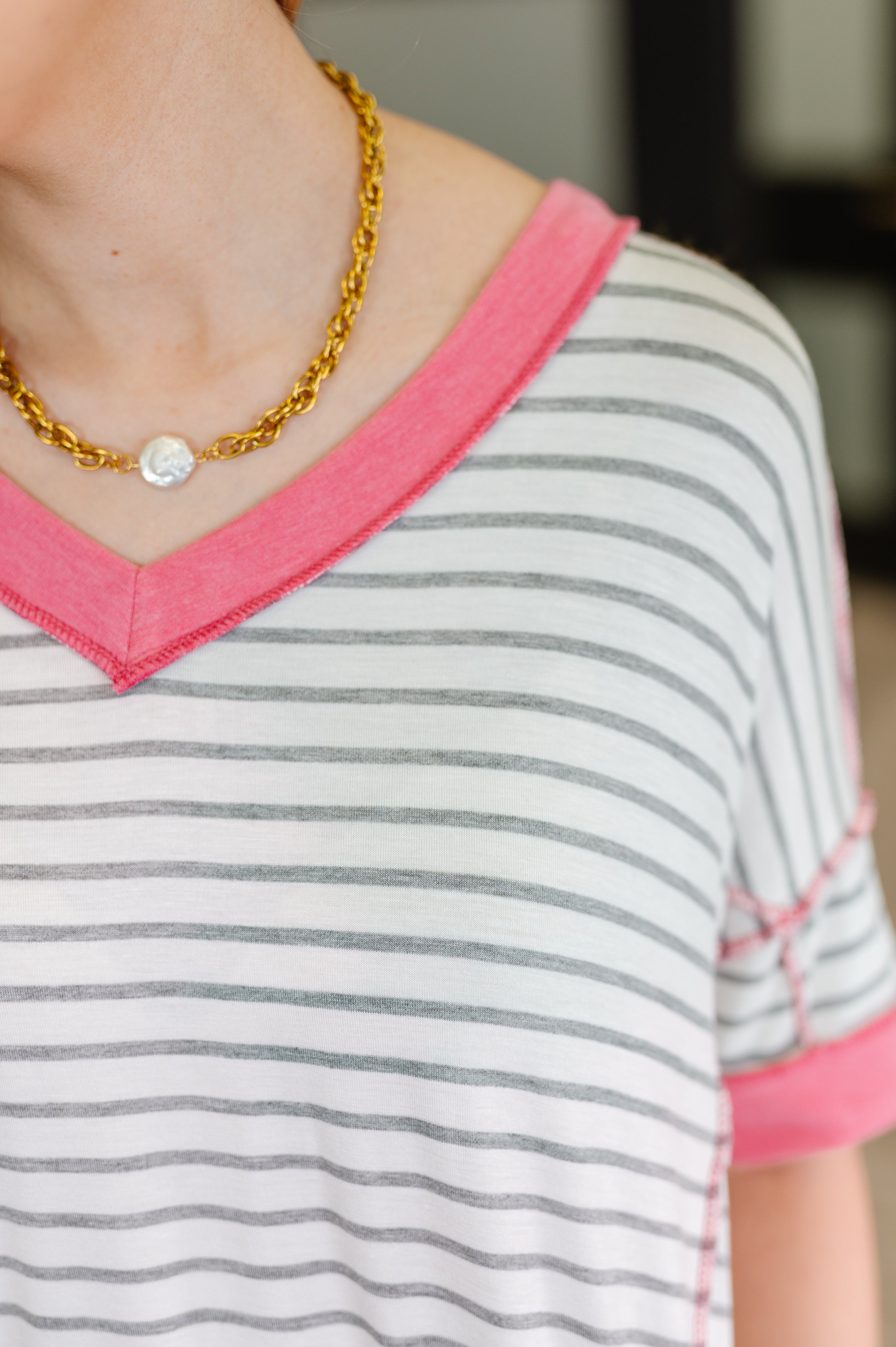 Close-up of striped ivory V-neck top with coral pink trim and rolled sleeves worn with gold chain necklace