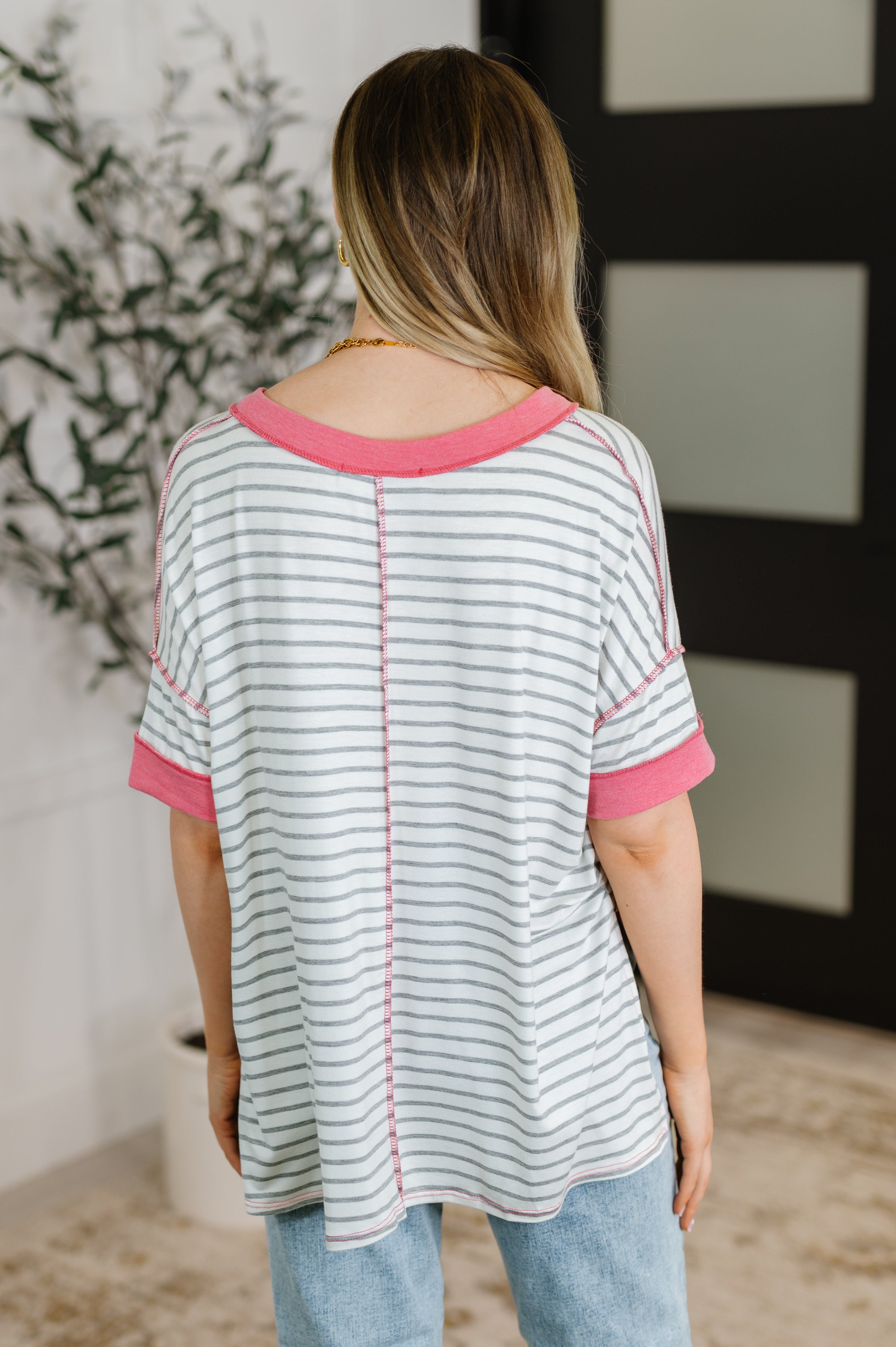Back view of woman wearing ivory striped V-neck top with pink trim on sleeves and neckline indoors