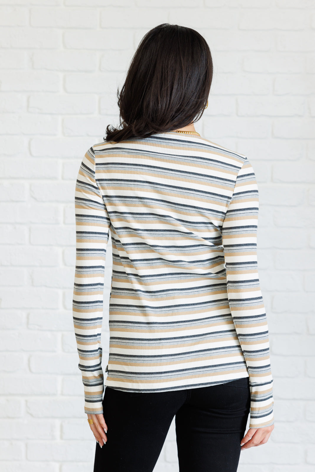 Woman wearing a ribbed knit top with horizontal tan, blue, and white stripes and long sleeves indoors