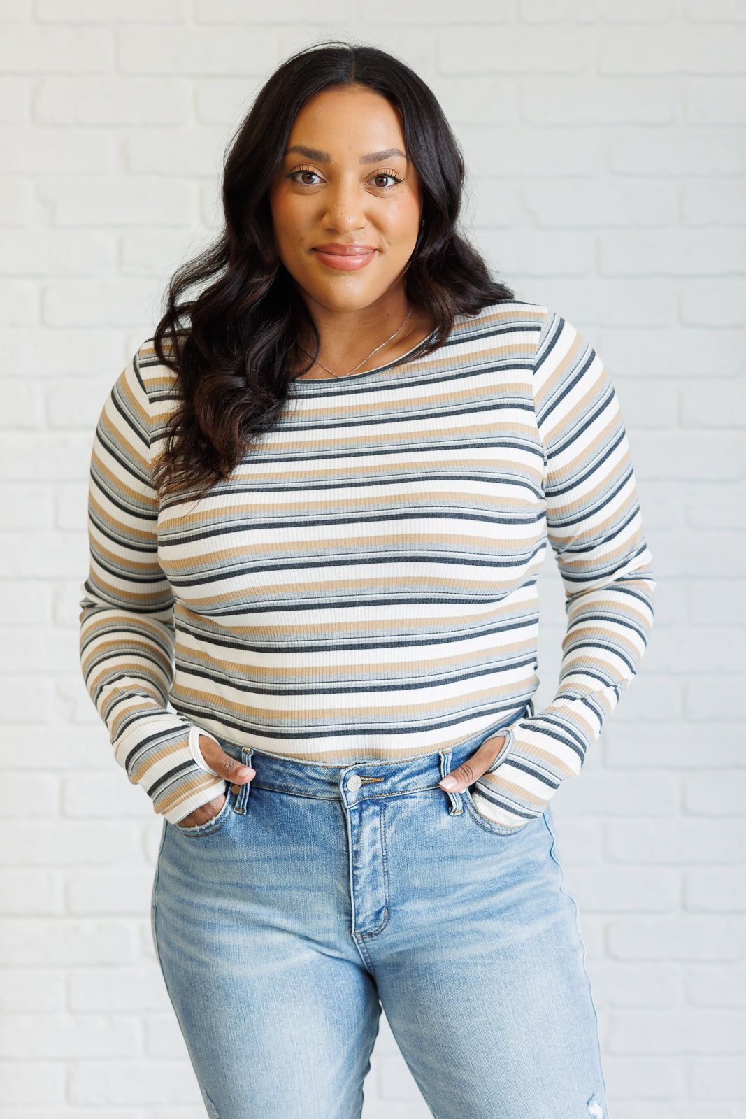 Woman wearing a long-sleeve ribbed knit striped top with thumbholes paired with light blue high-rise jeans indoors