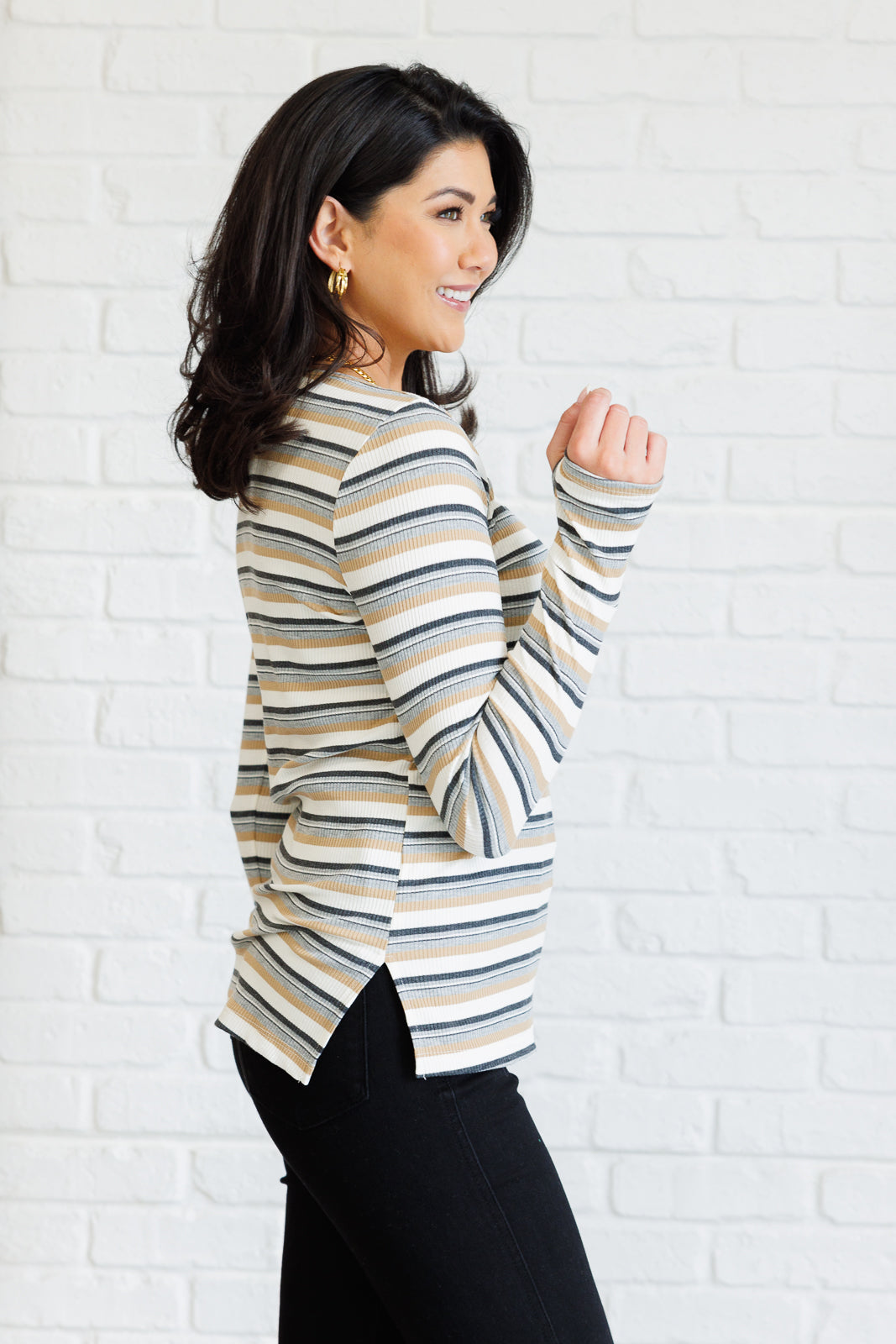 Woman wearing a ribbed knit striped long-sleeve top with thumbholes and side slits paired with black pants indoors