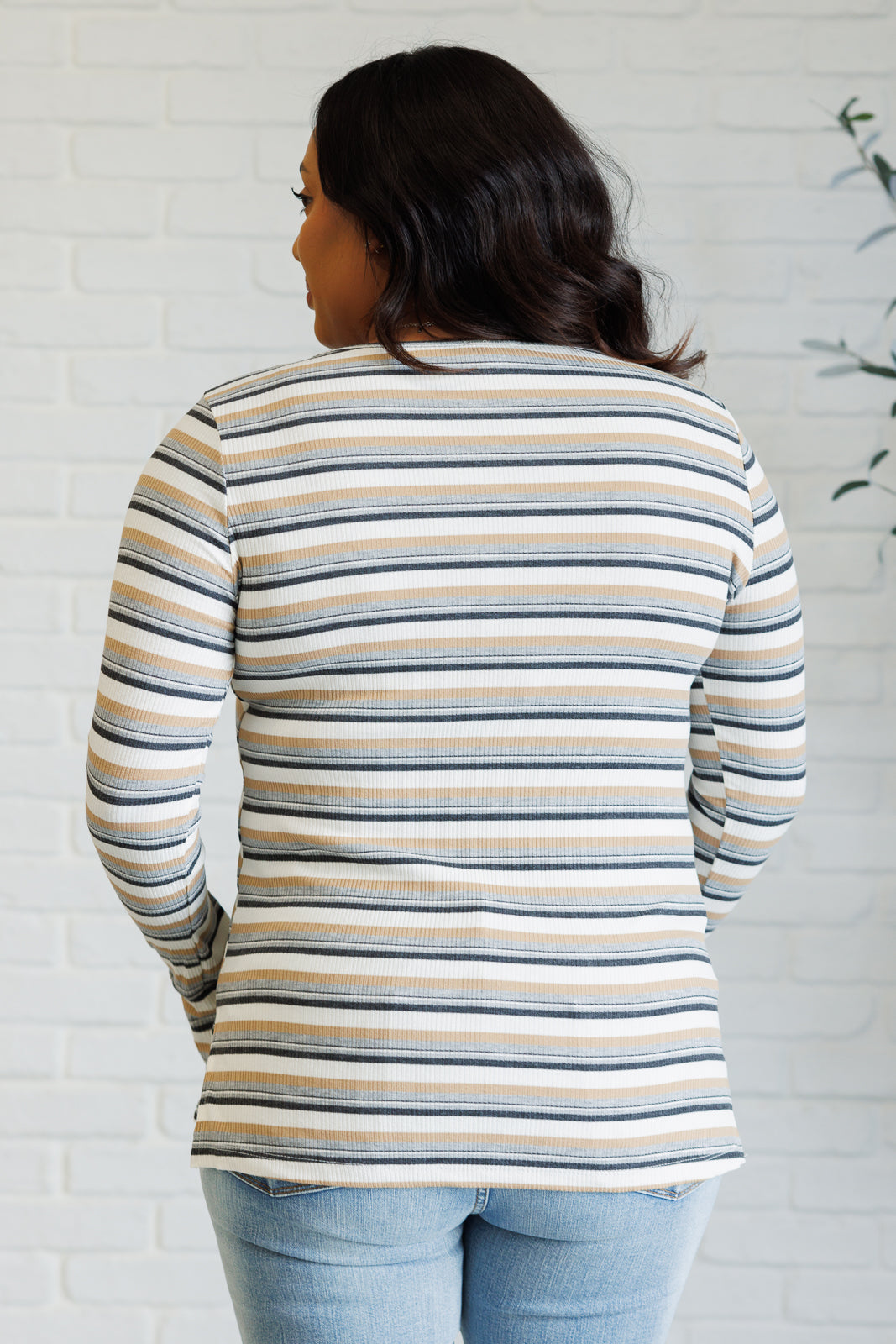 Back view of woman wearing a blue and cream ribbed striped long-sleeve top with a round neckline indoors