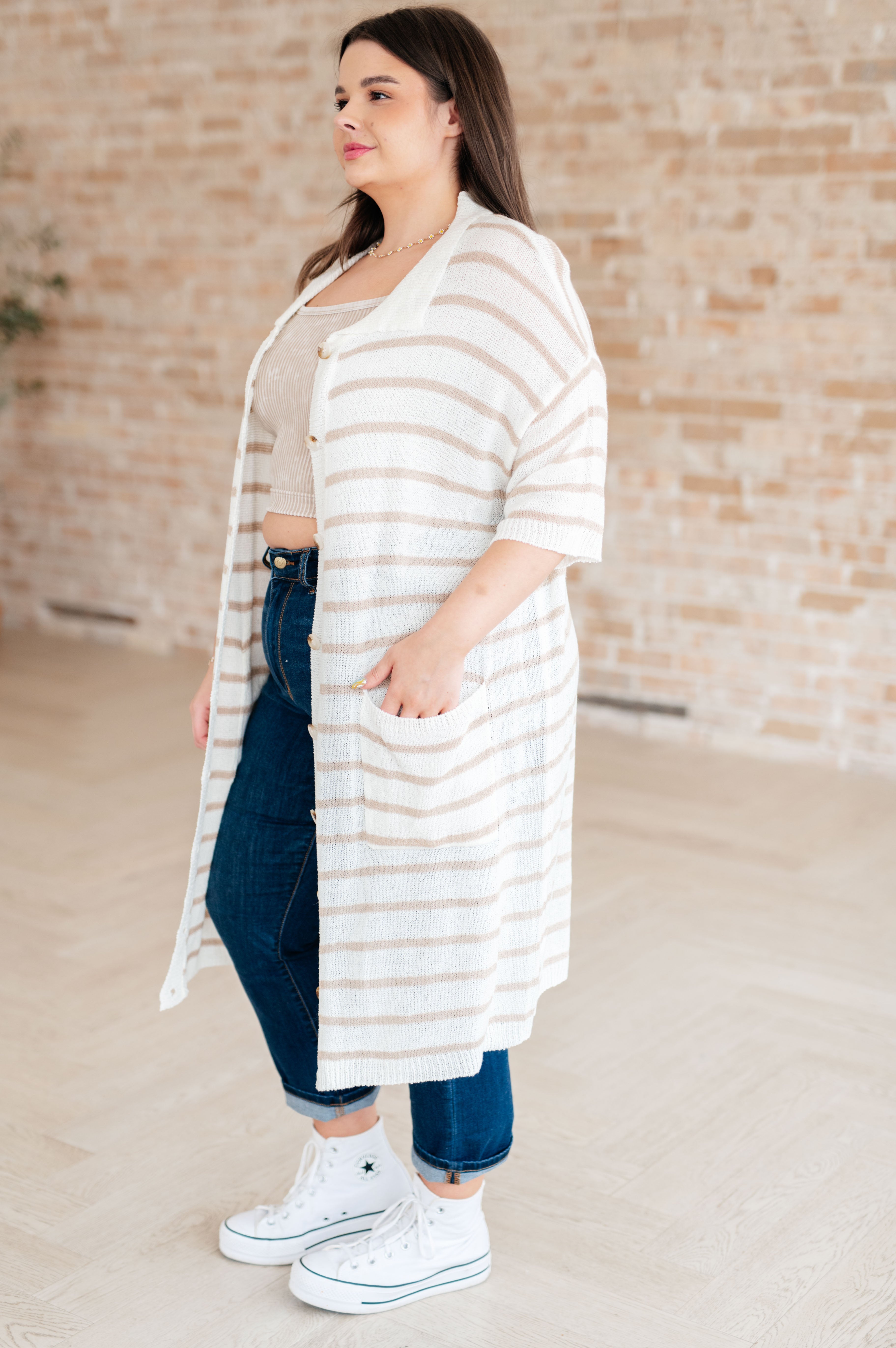 Woman wearing beige and white striped long button-up cardigan with short sleeves and pockets indoors