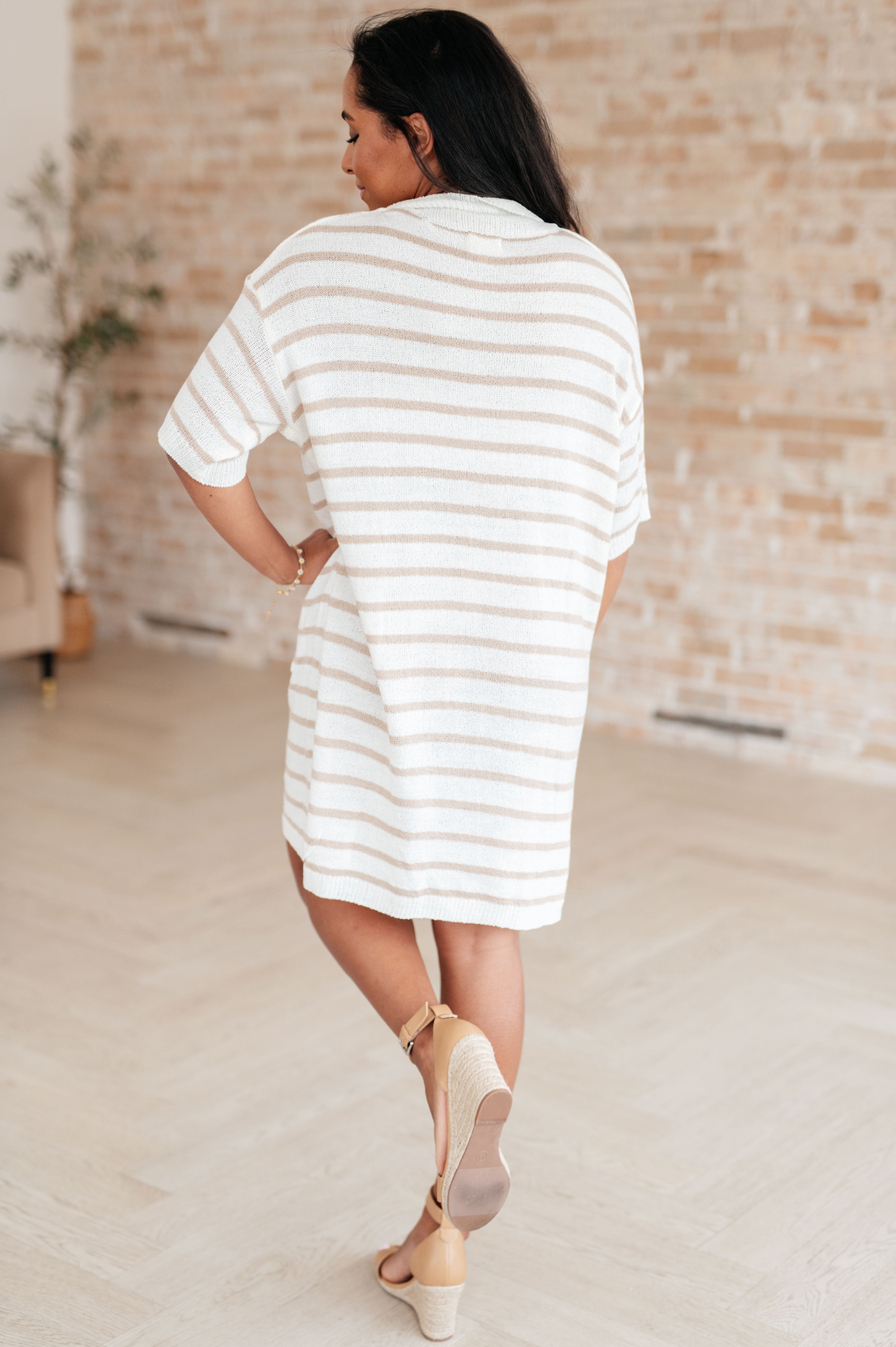Woman wearing loose fit white and beige striped button-up collared dress with short sleeves walking indoors