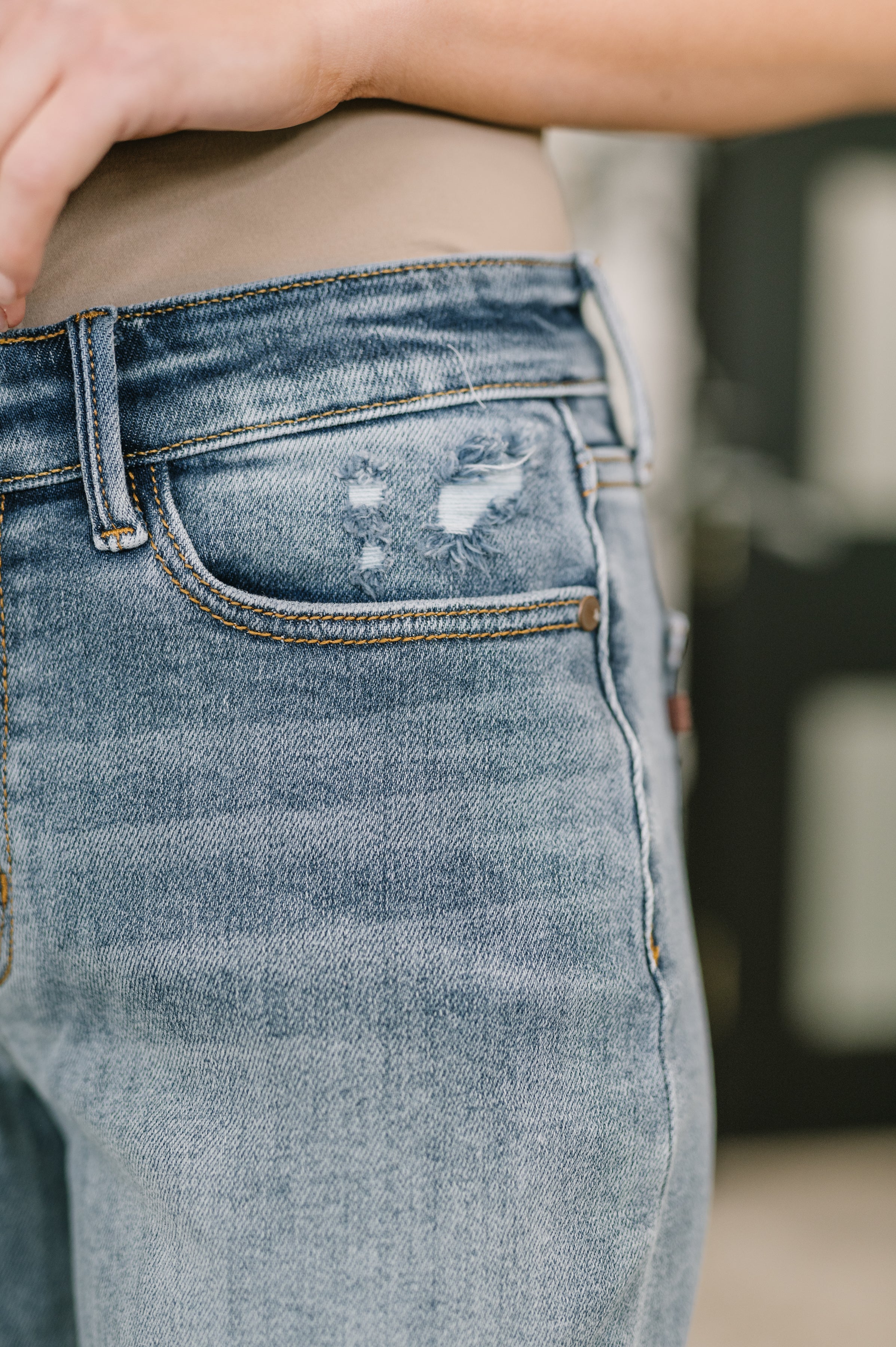 Close-up of blue denim jeans with light distressing on the front pocket area and visible stitching details