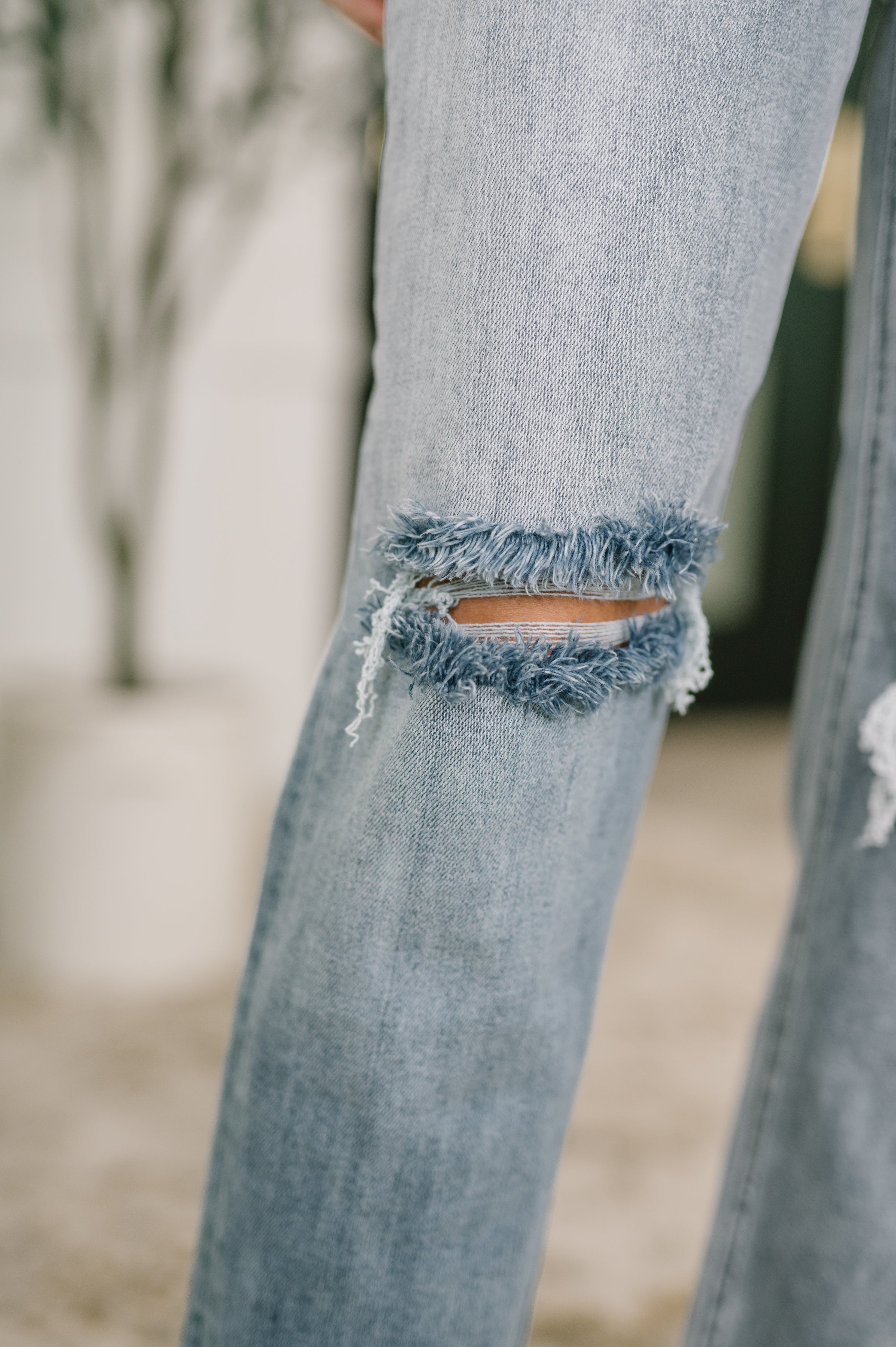 Close-up of blue denim pants with a frayed ripped detail on the knee area showing fabric texture