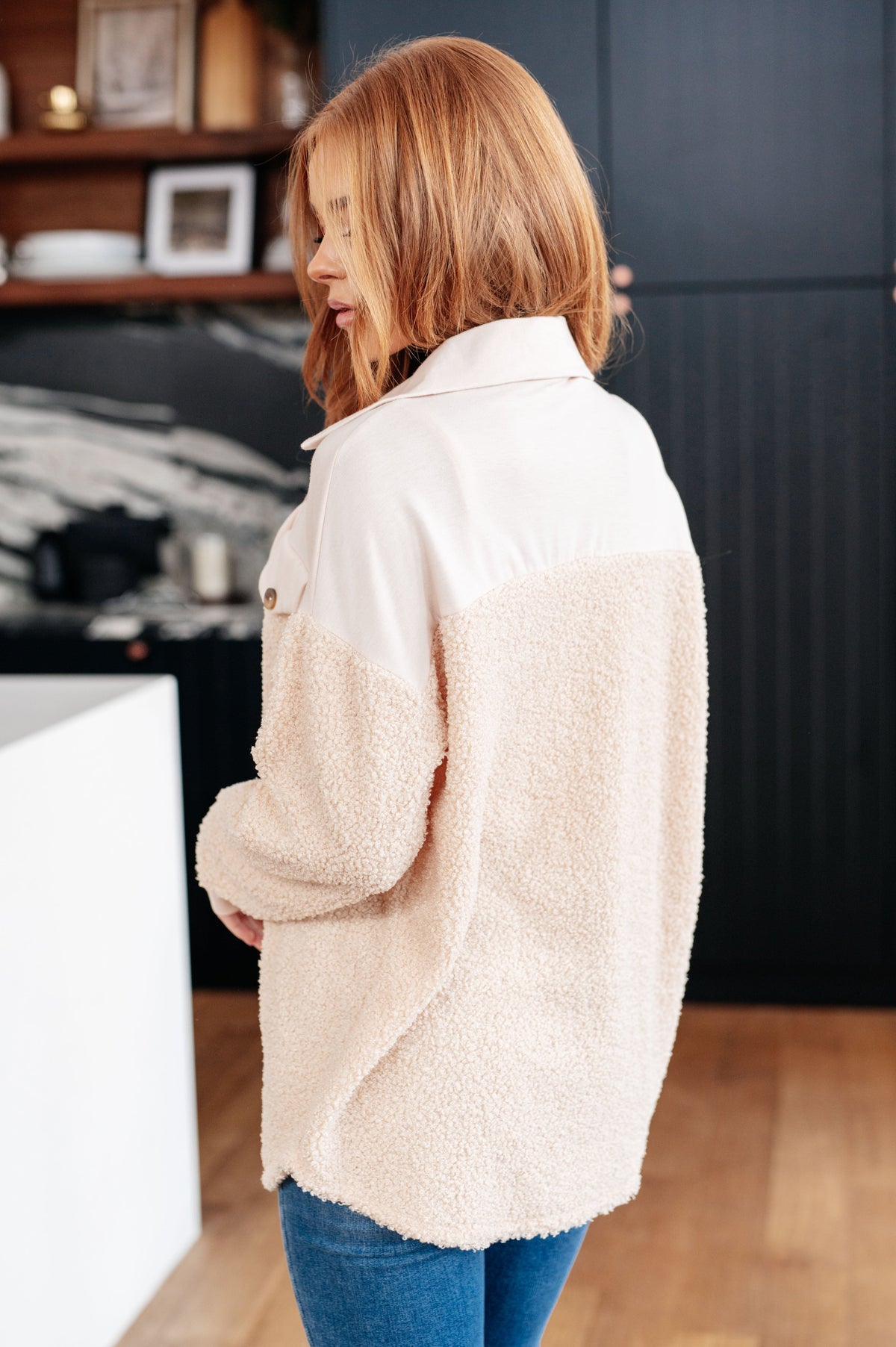 Woman viewed from behind wearing a cream sherpa shacket with a smooth jersey knit yoke and cozy fleece body over blue jeans