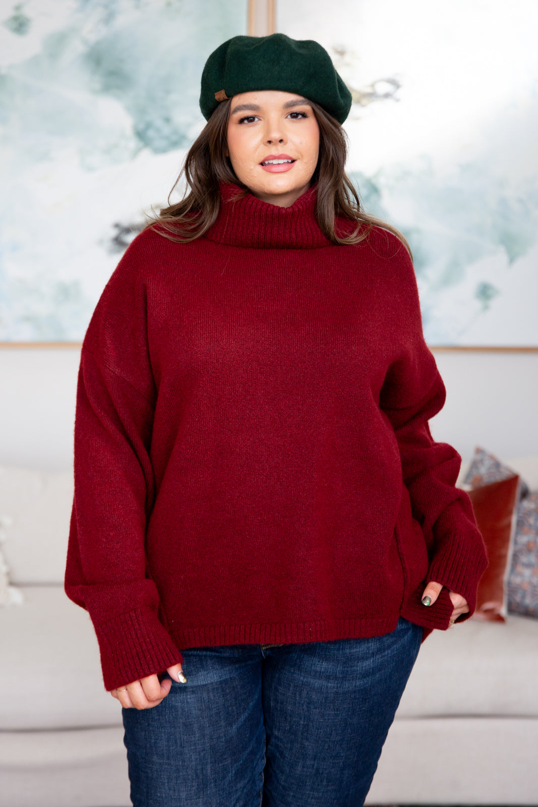 Woman wearing oversized deep red turtleneck sweater with long sleeves and green beret indoors