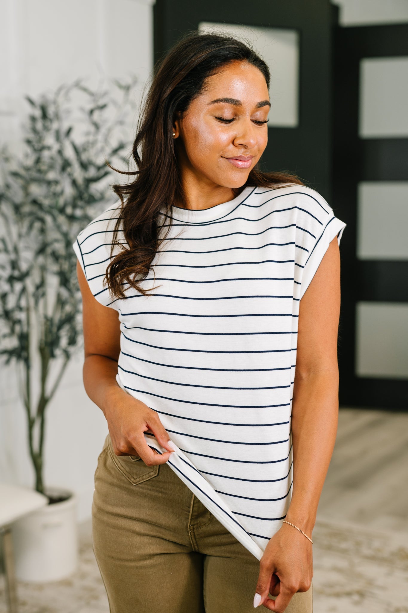 Woman wearing ivory striped cap sleeve tee with relaxed fit paired with olive pants in a bright eclectic space