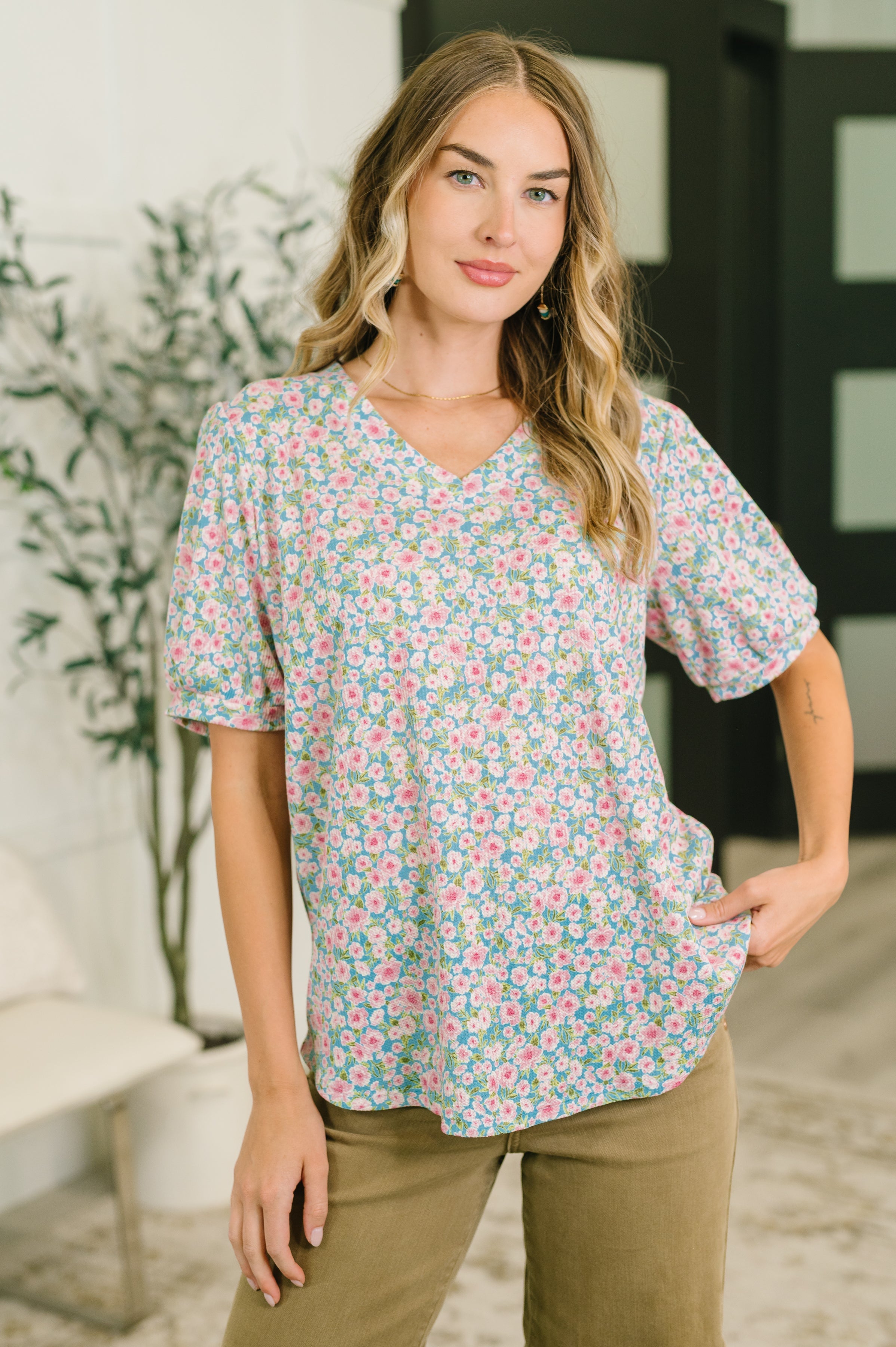 Woman wearing blue floral blouse with puff sleeves and V-neck paired with olive pants indoors