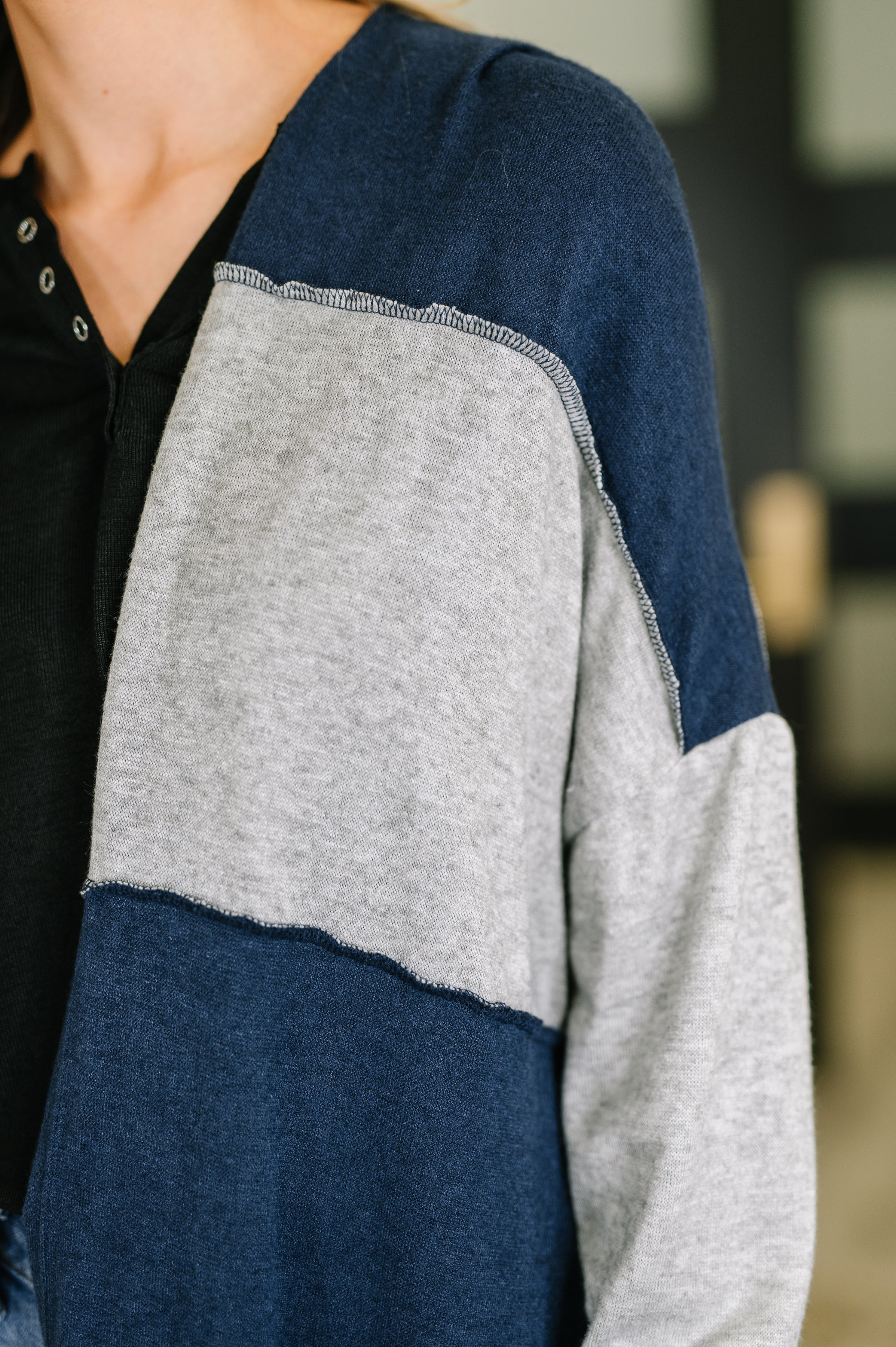 Close-up of soft knit open front cardigan with navy and light gray color block detailing on sleeve and shoulder