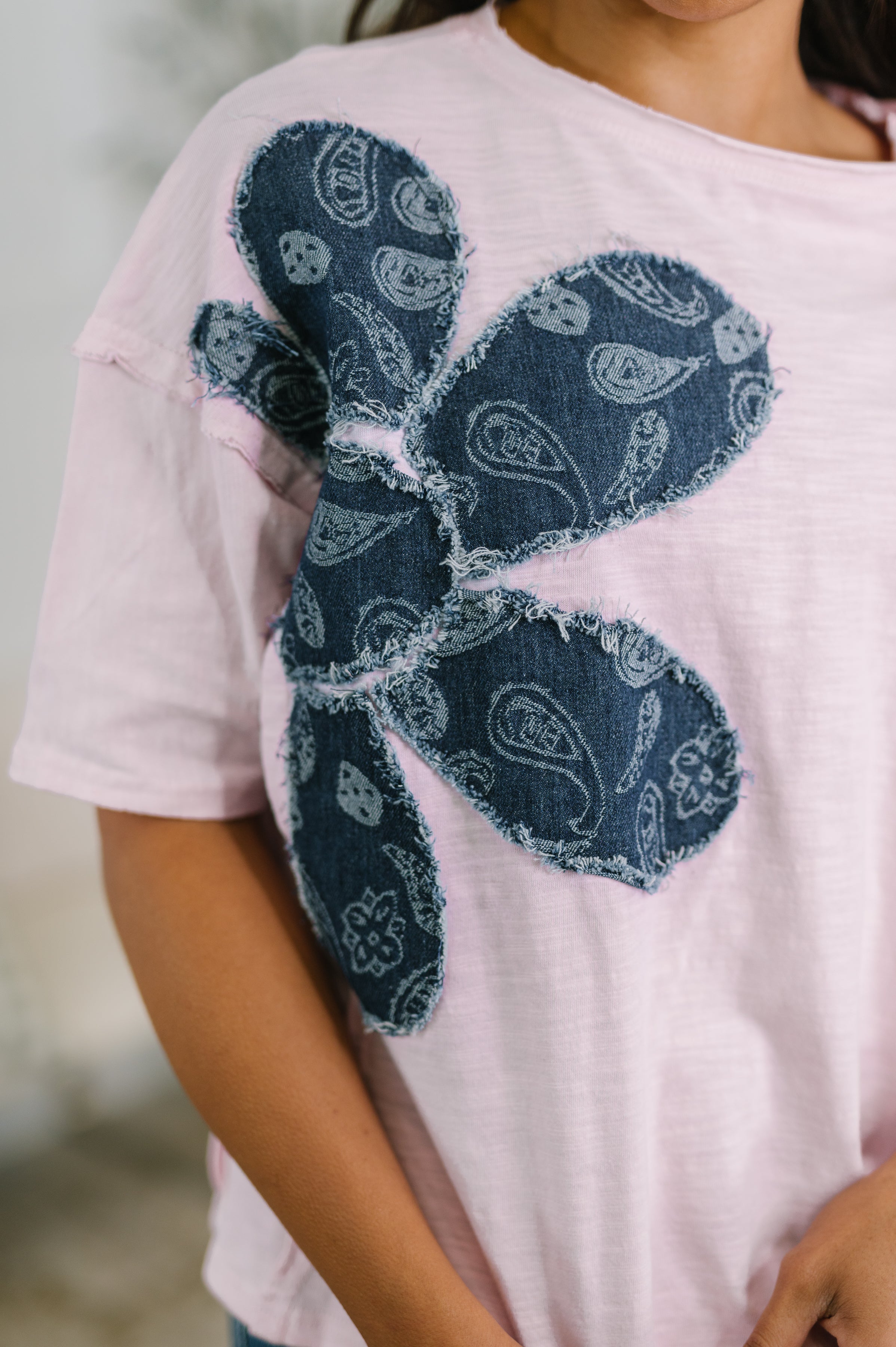 Close-up of pink knit top with large frayed dark paisley floral applique on front near shoulder and sleeve