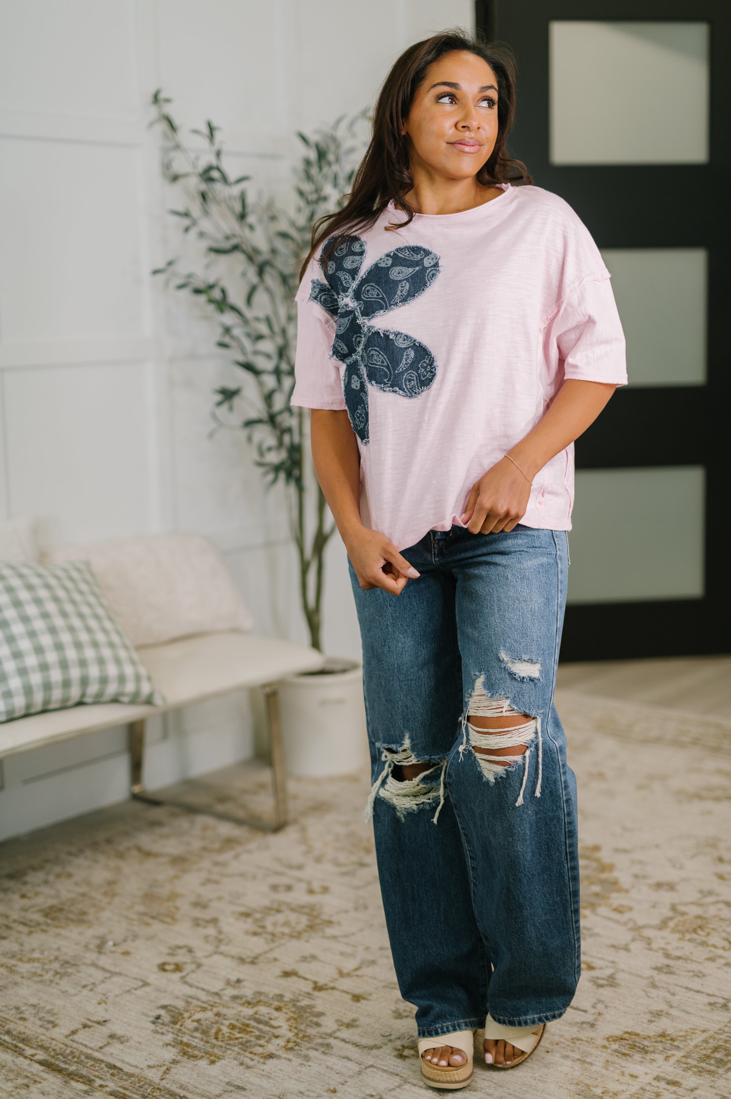 Woman wearing a pink top with dark blue paisley floral design paired with ripped relaxed fit jeans and sandals indoors