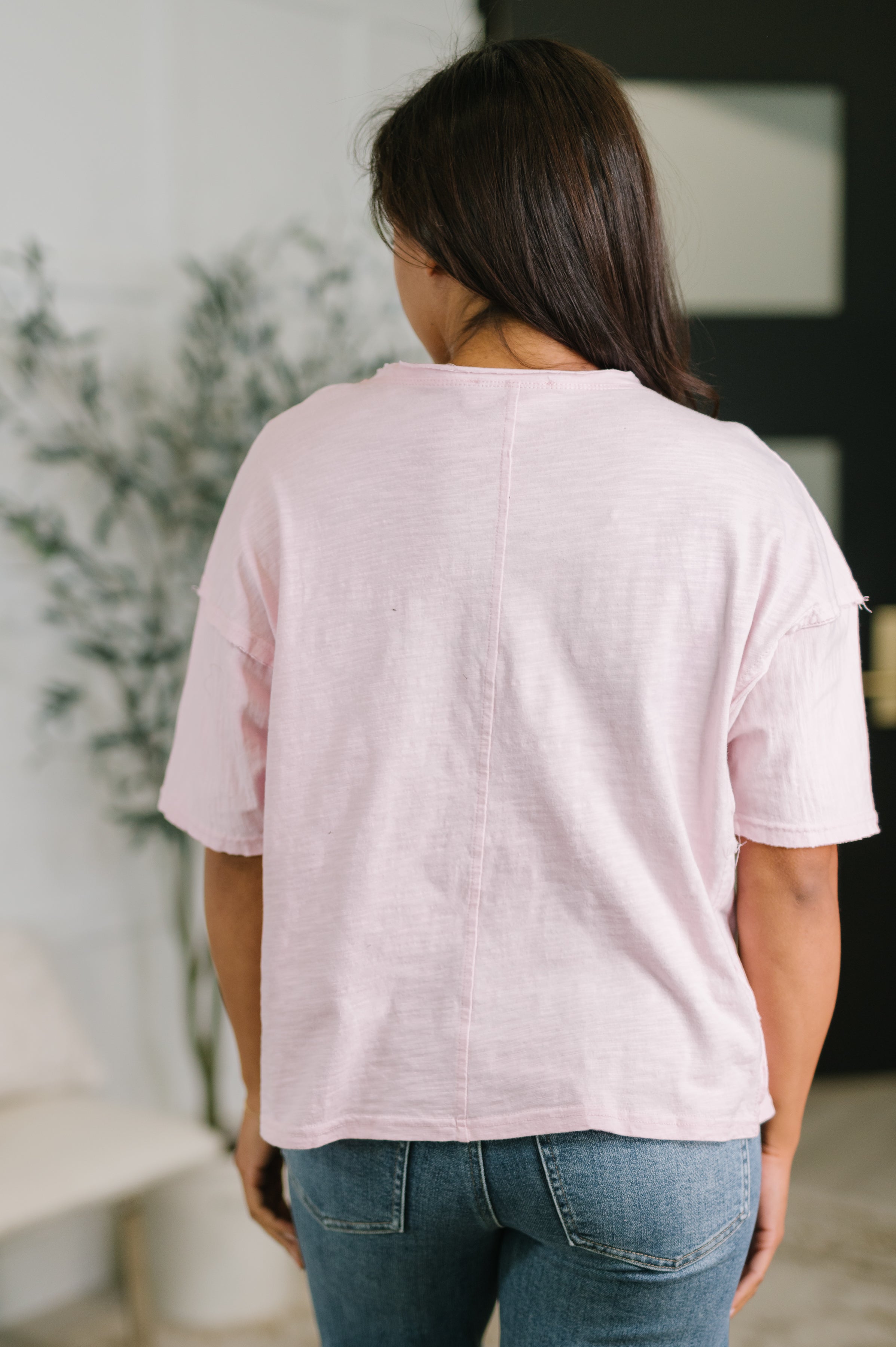 Back view of woman wearing a relaxed pink drop shoulder knit top with short sleeves and seam detail indoors