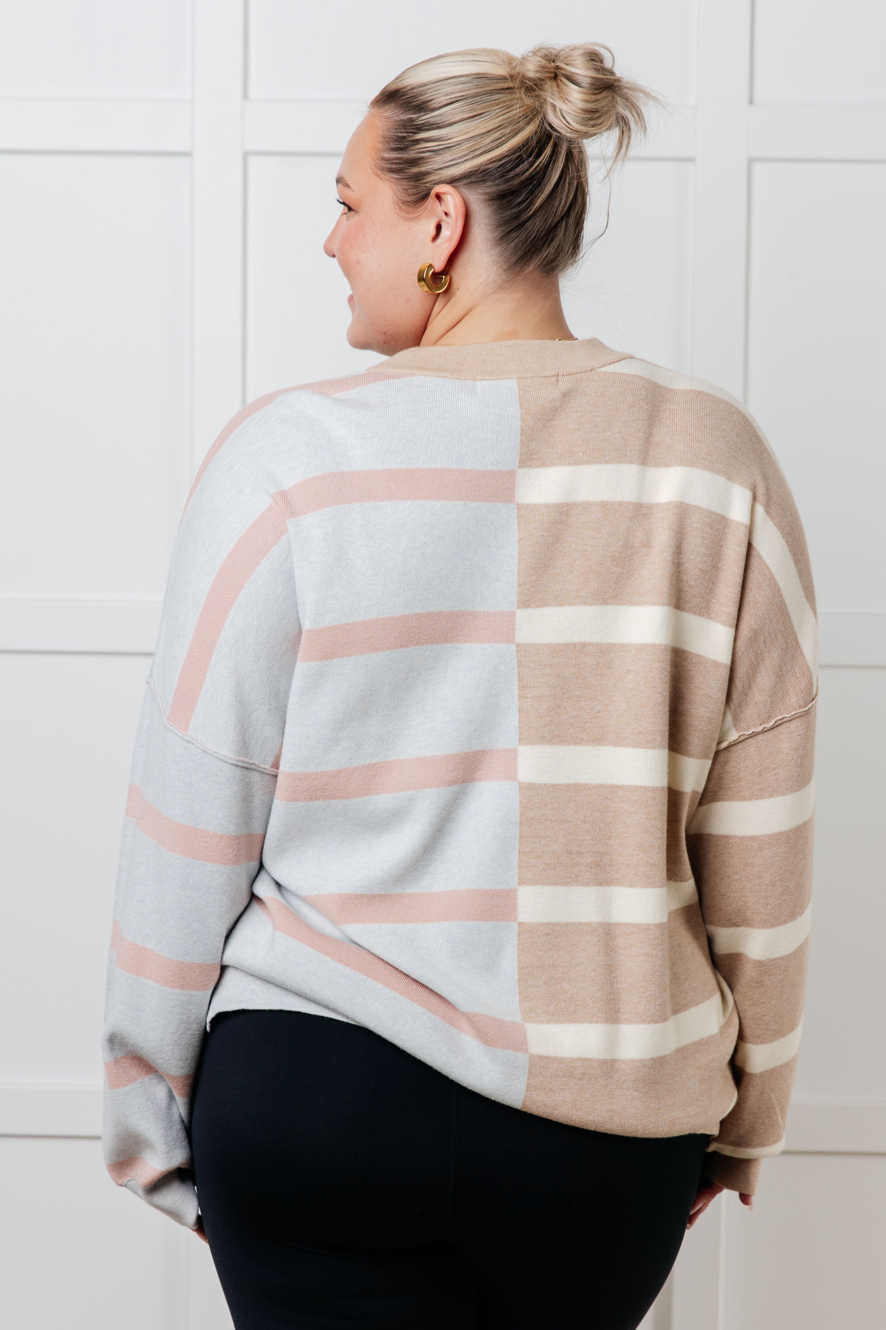 Woman wearing oversized striped patchwork sweater with beige and light gray blocks indoors