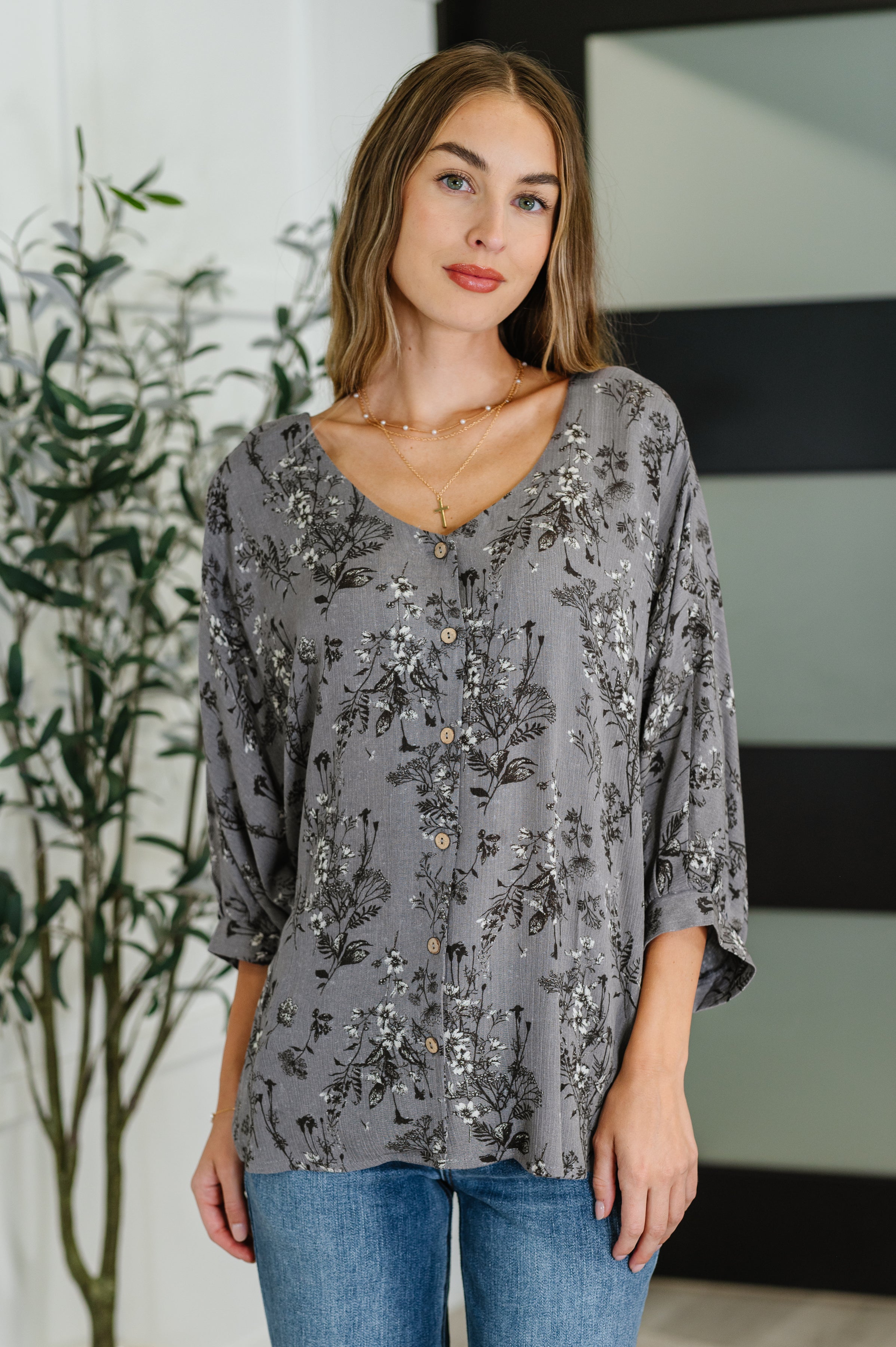Woman wearing loose dune grey crinkle blouse with black and white botanical print and natural buttons indoors