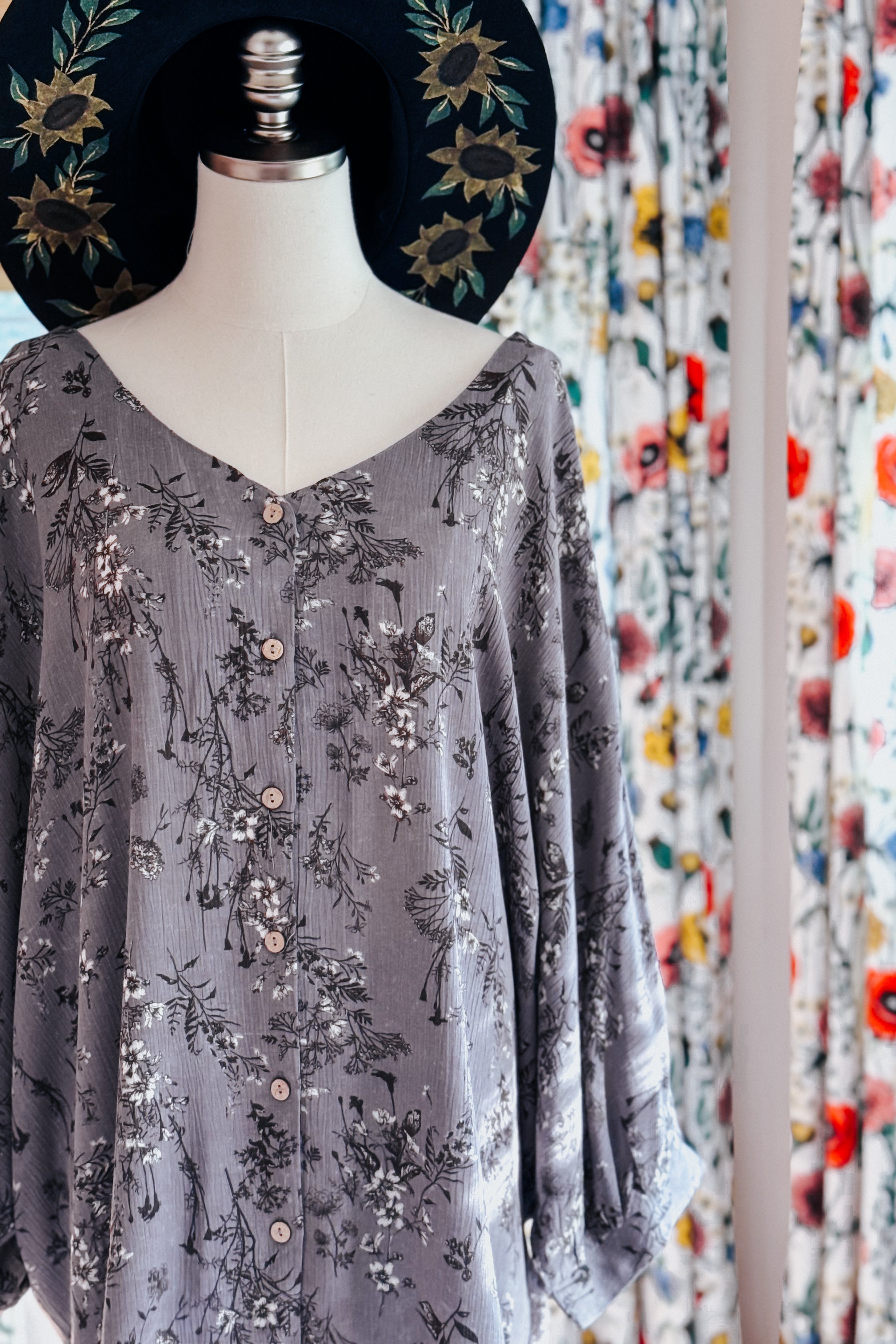 Dune grey crinkle blouse with delicate black and white floral print buttoned front displayed on mannequin with black floral hat