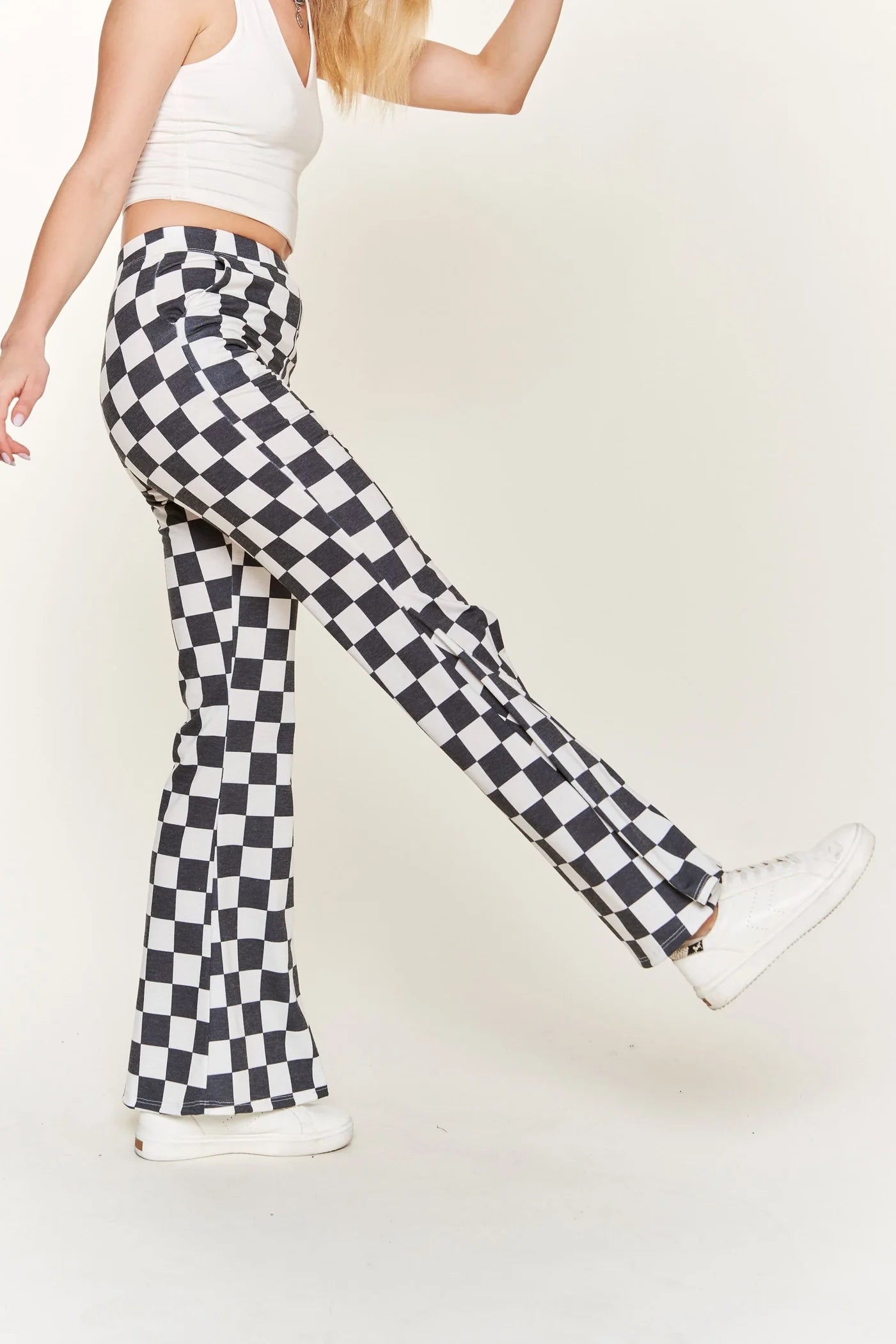 Woman wearing black and white checkered flared pants and white sneakers posing against plain background