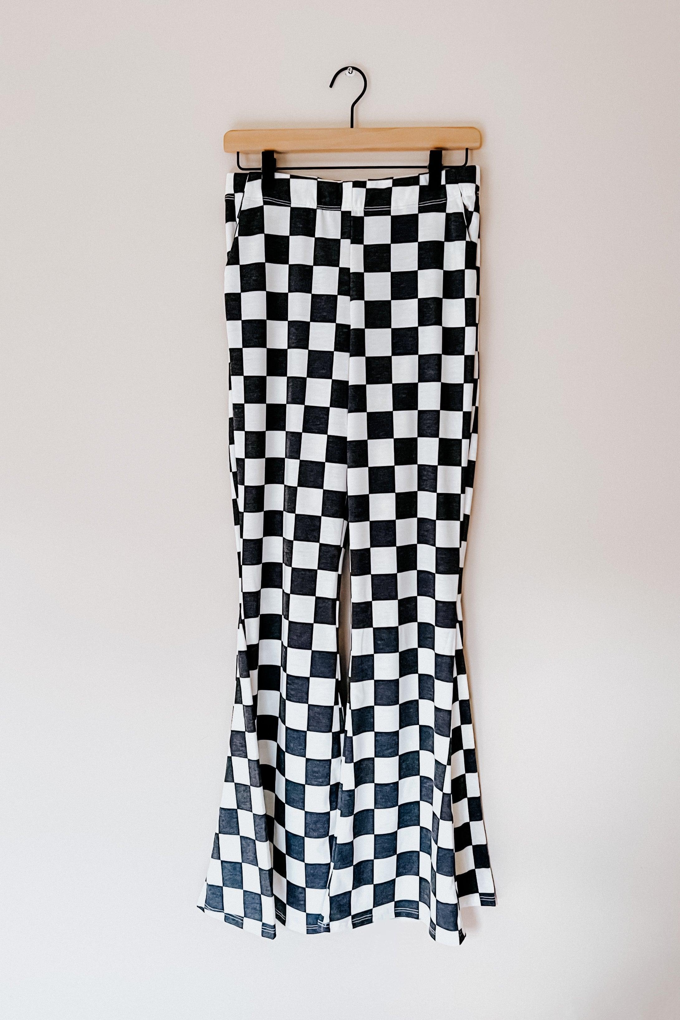 Black and white checkered flared pants hanging on wooden hanger against plain wall background