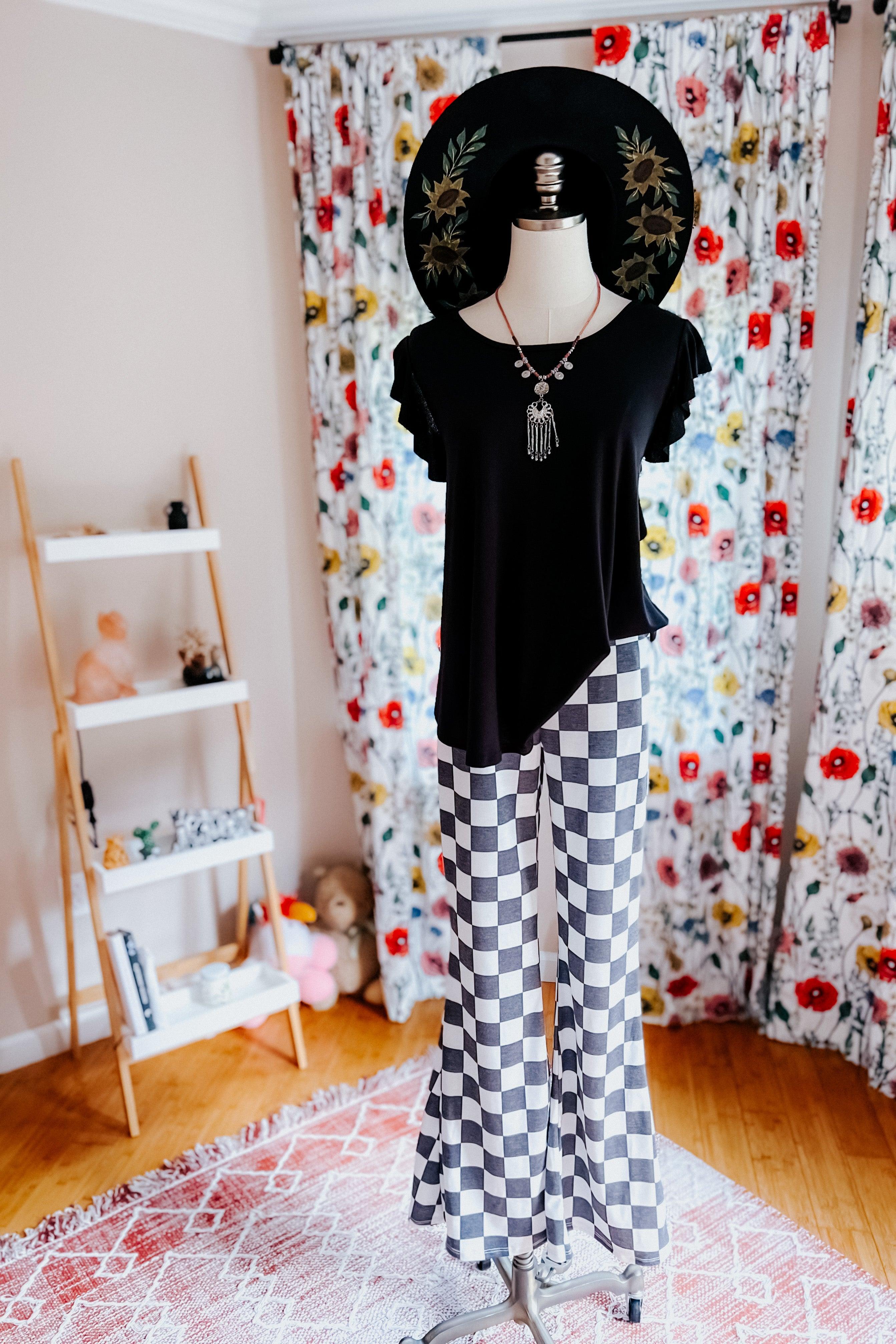 Mannequin dressed in black top and black and white checkered flared pants with floral embroidered black wide-brim hat indoors