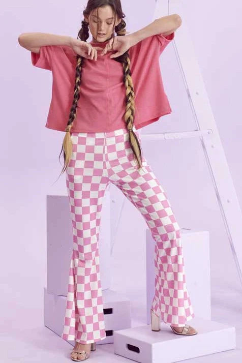 Woman wearing pink and white checkerboard flared pants with pink loose top posing against pastel purple background