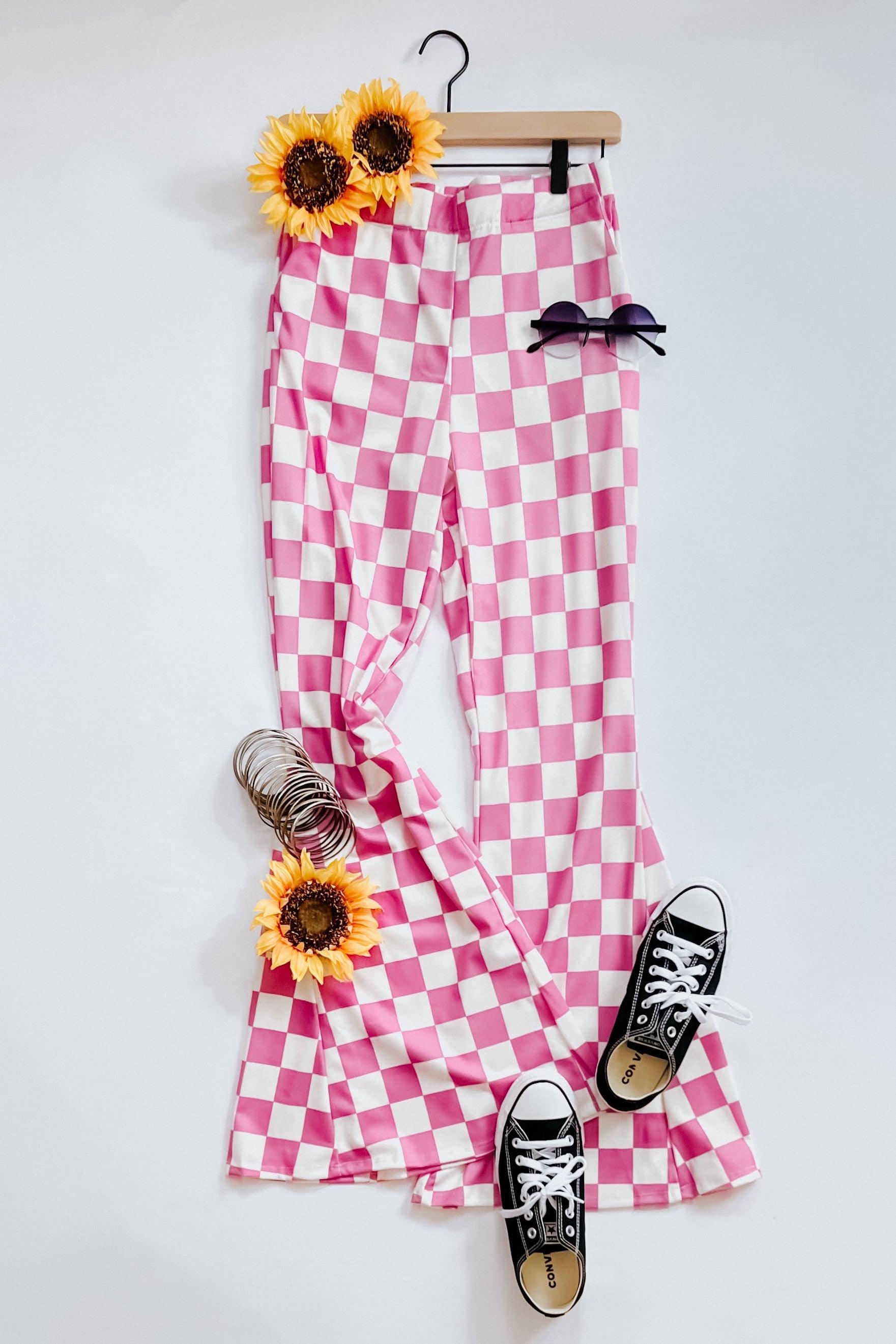 Pink and white checkered flared pants styled with black sneakers, round sunglasses, and sunflower accessories on white background