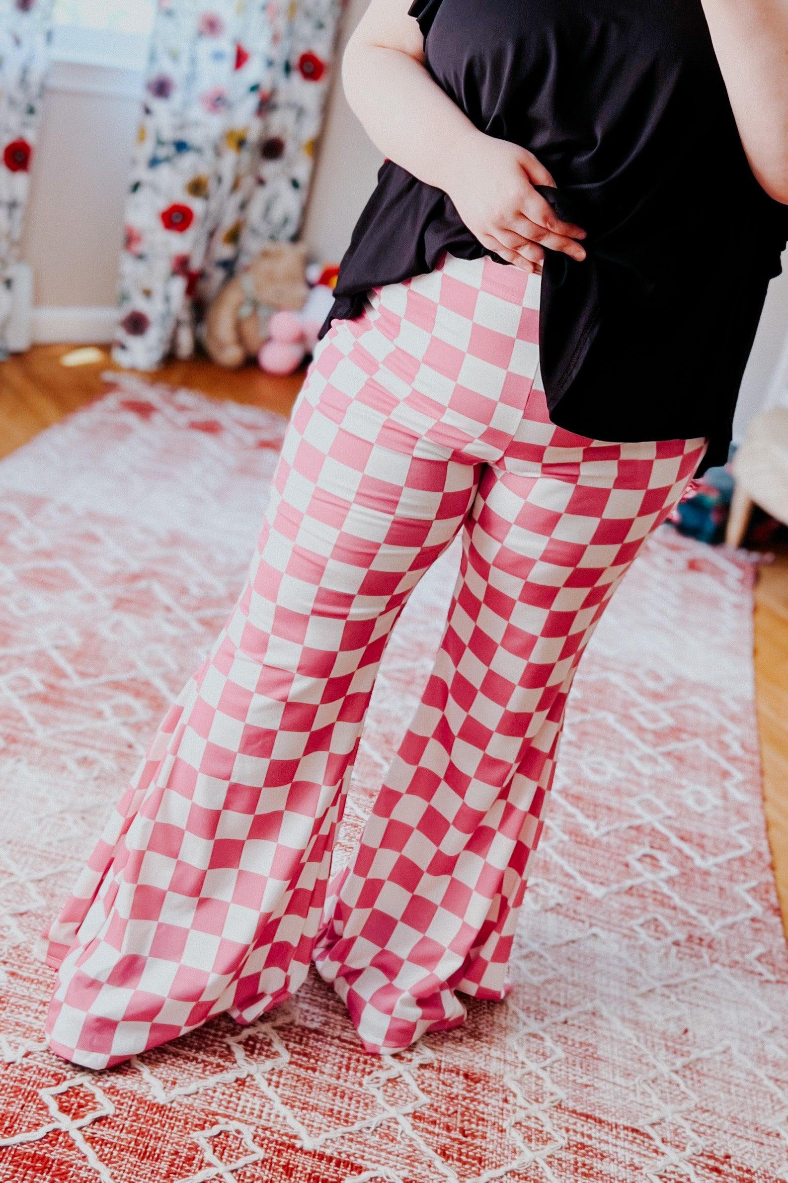 Woman wearing pink and white checkered flared pants lifting black top standing on patterned rug indoors