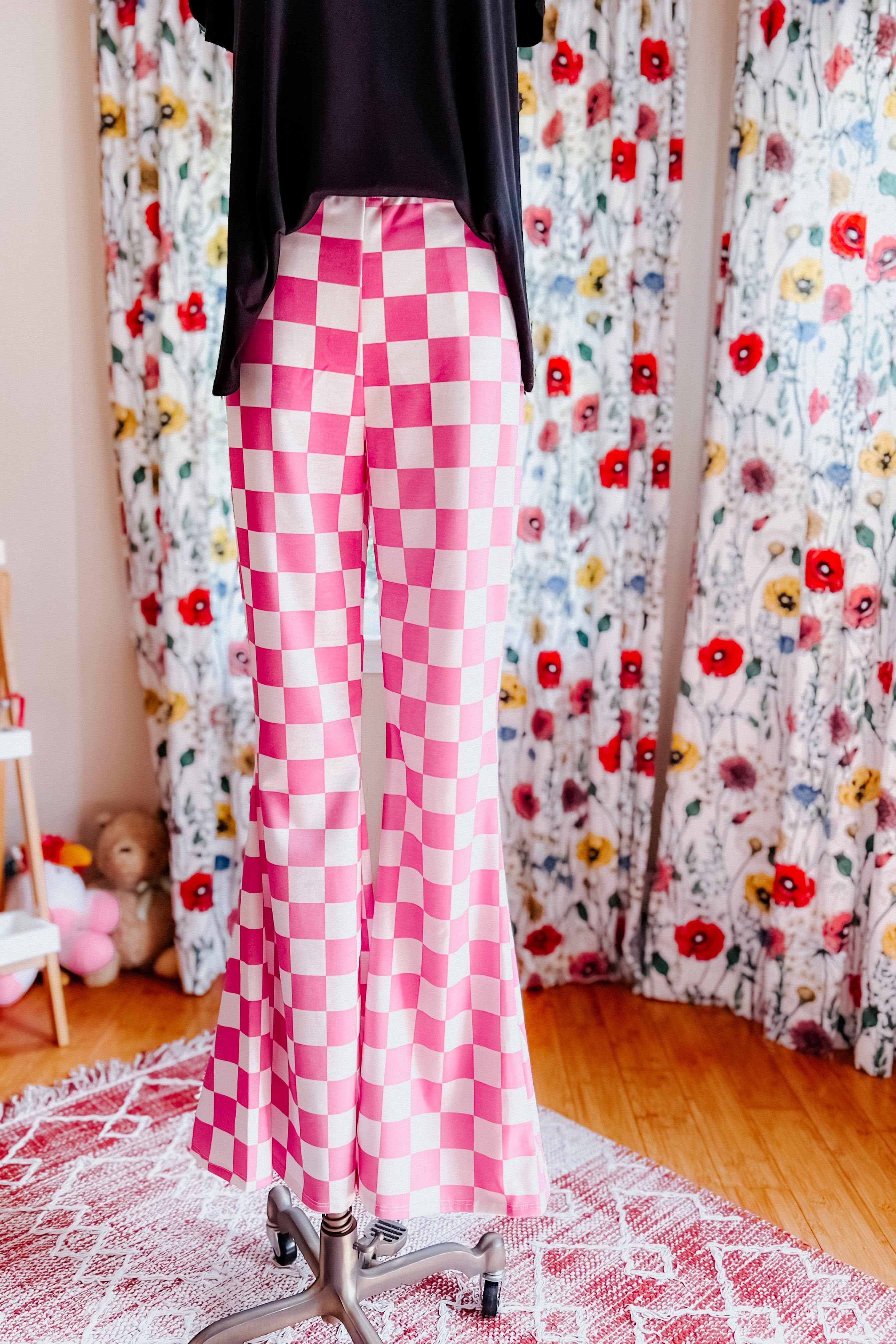 Pink and white checkered flared pants displayed on a mannequin in a bright room with floral curtains and wooden floor