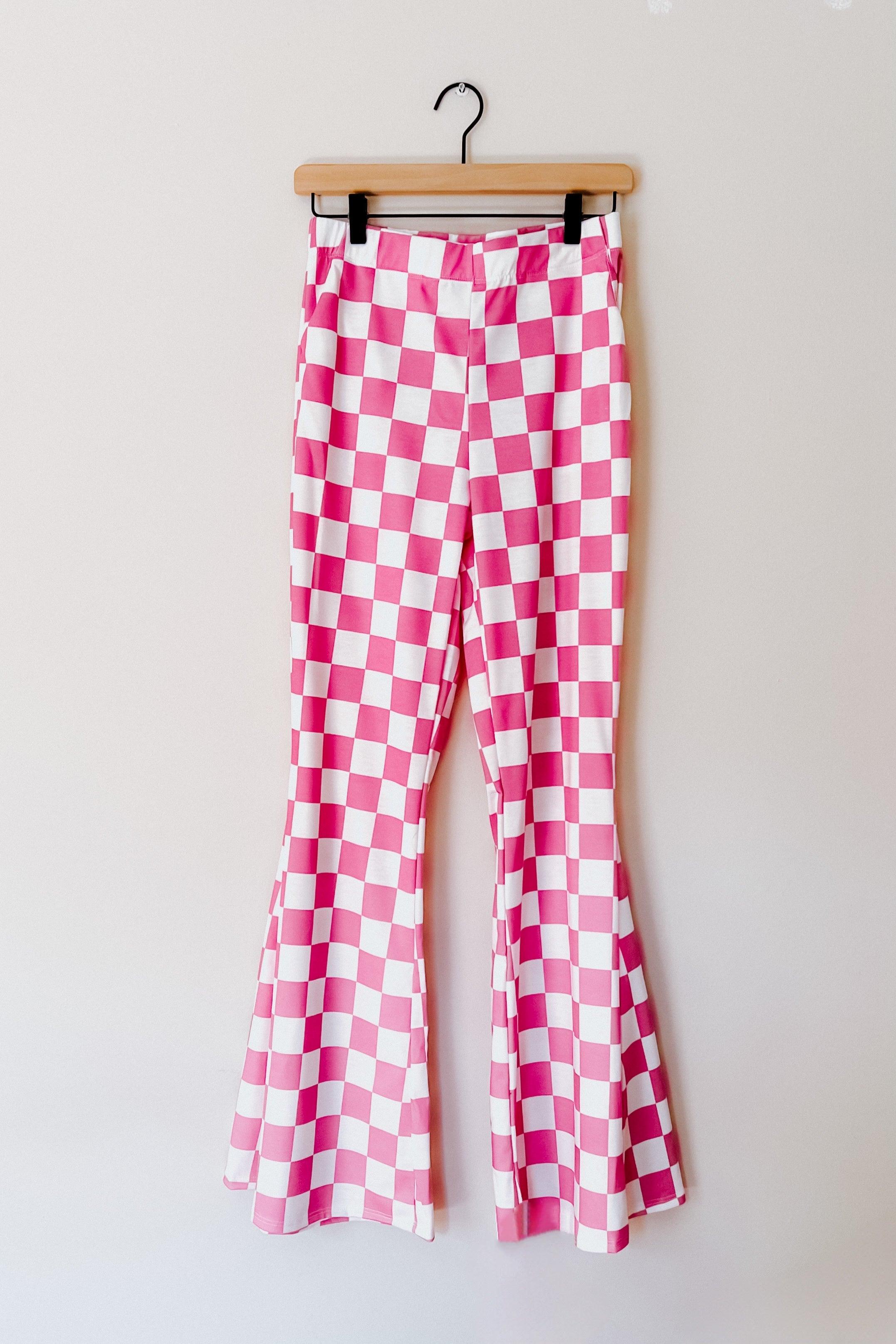 Pink and white checkered flared pants hanging on wooden hanger against plain wall background