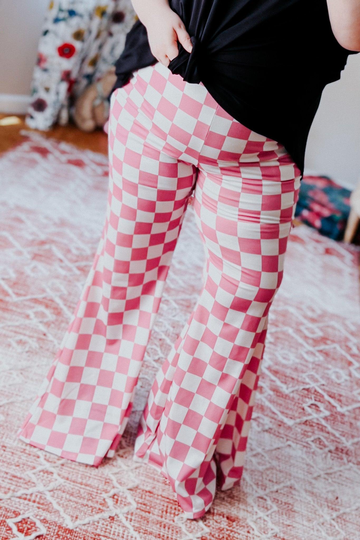 Woman wearing pink and white checkered flared pants paired with black top standing on patterned rug indoors