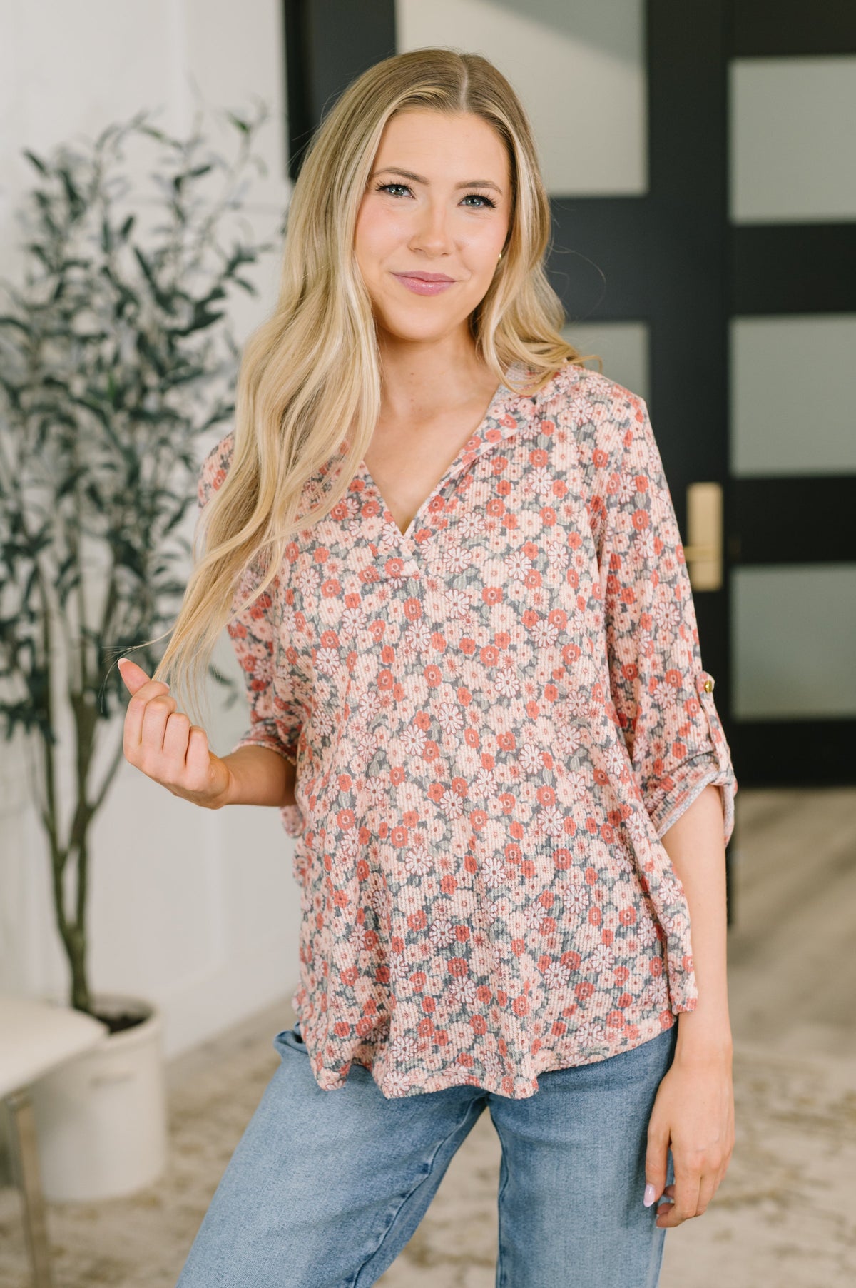Woman modeling a Peach floral split neck top with half sleeves and blue jeans in a bright modern home interior