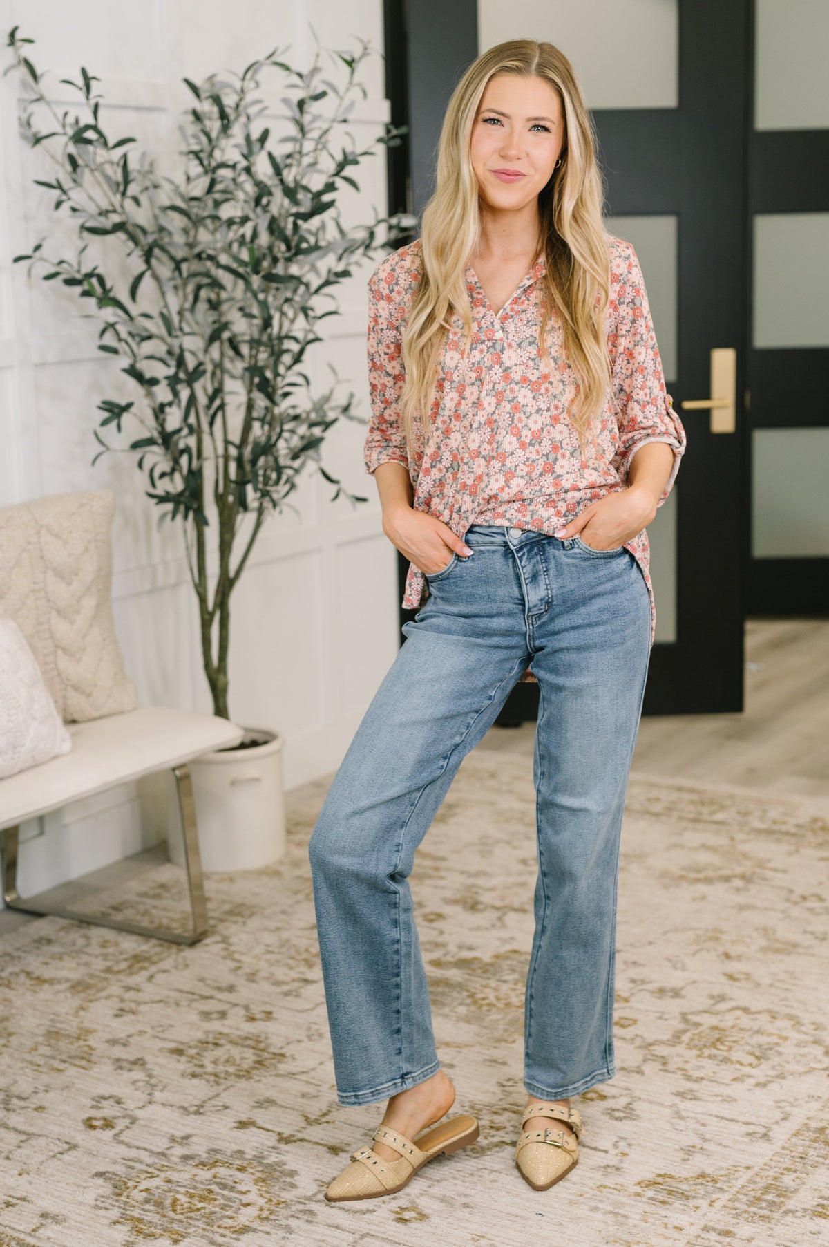 Woman modeling a peach floral split neck half sleeve top with relaxed jeans and woven flats in a bright home interior