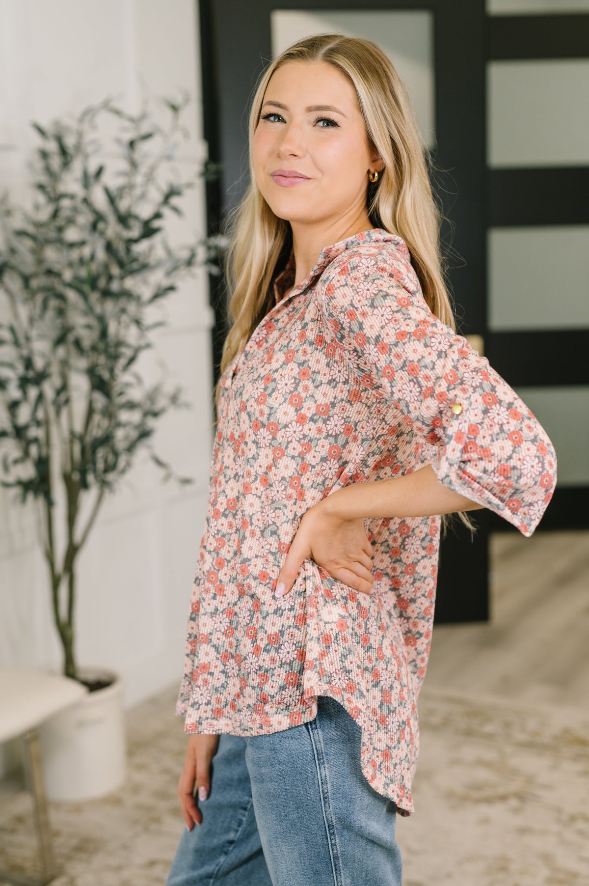 Woman modeling a peach floral split neck top with half sleeves and blue jeans in a bright modern interior