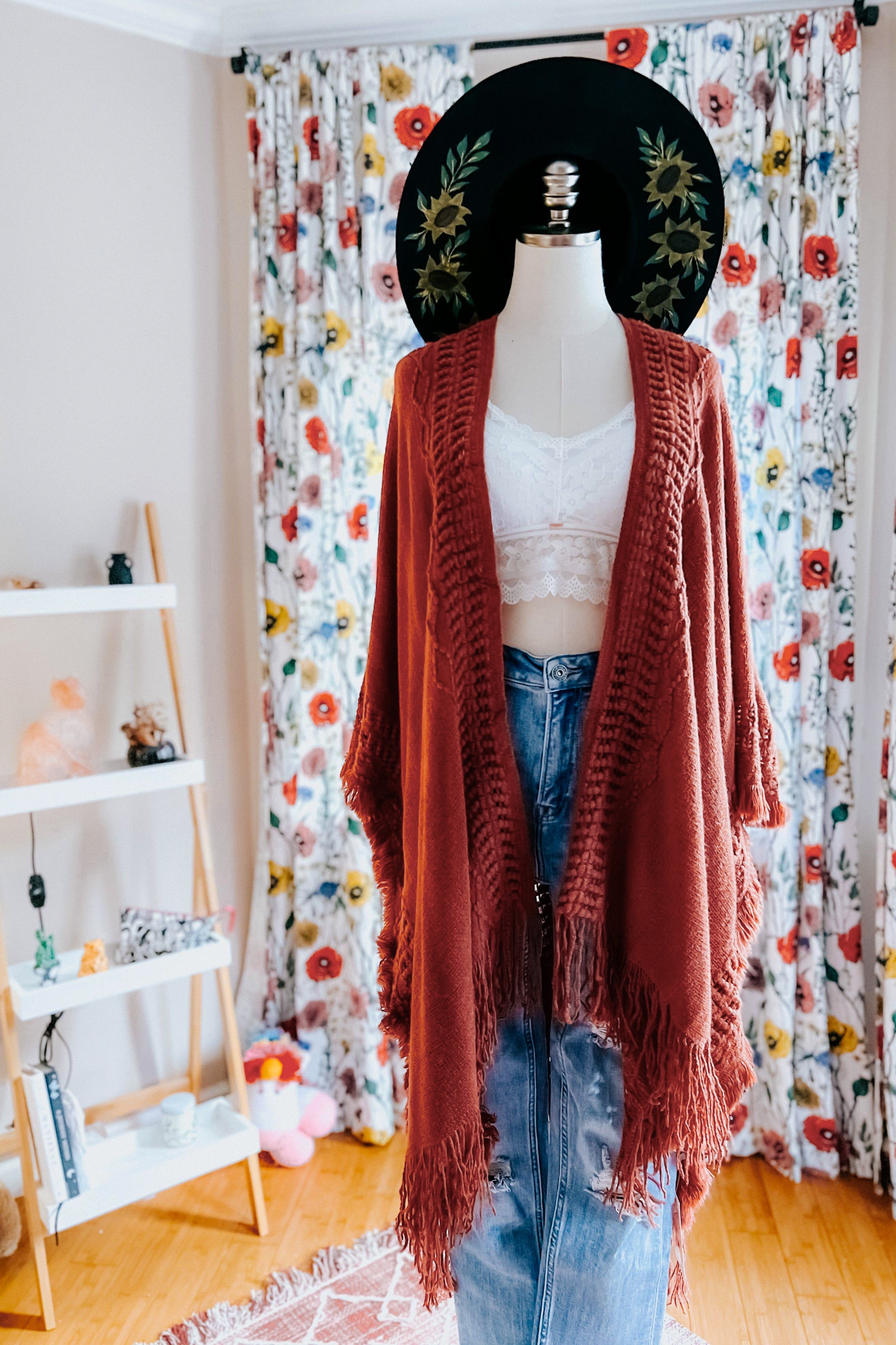 Mannequin dressed in rust-colored fringed bohemian ruana layered over lace crop top and denim skirt in eclectic room setting