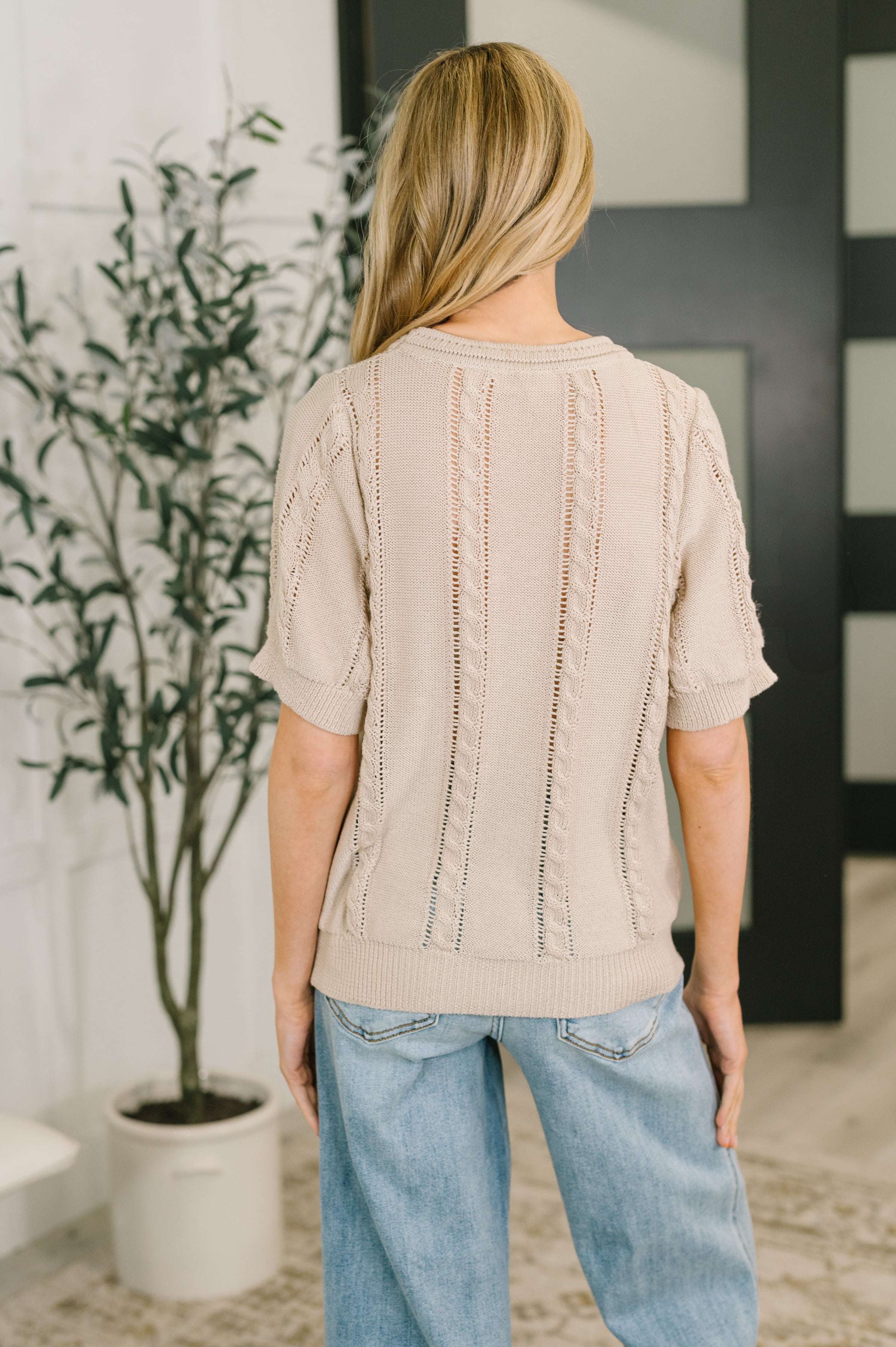 Back view of woman wearing beige embroidered knit top with light blue relaxed fit jeans indoors