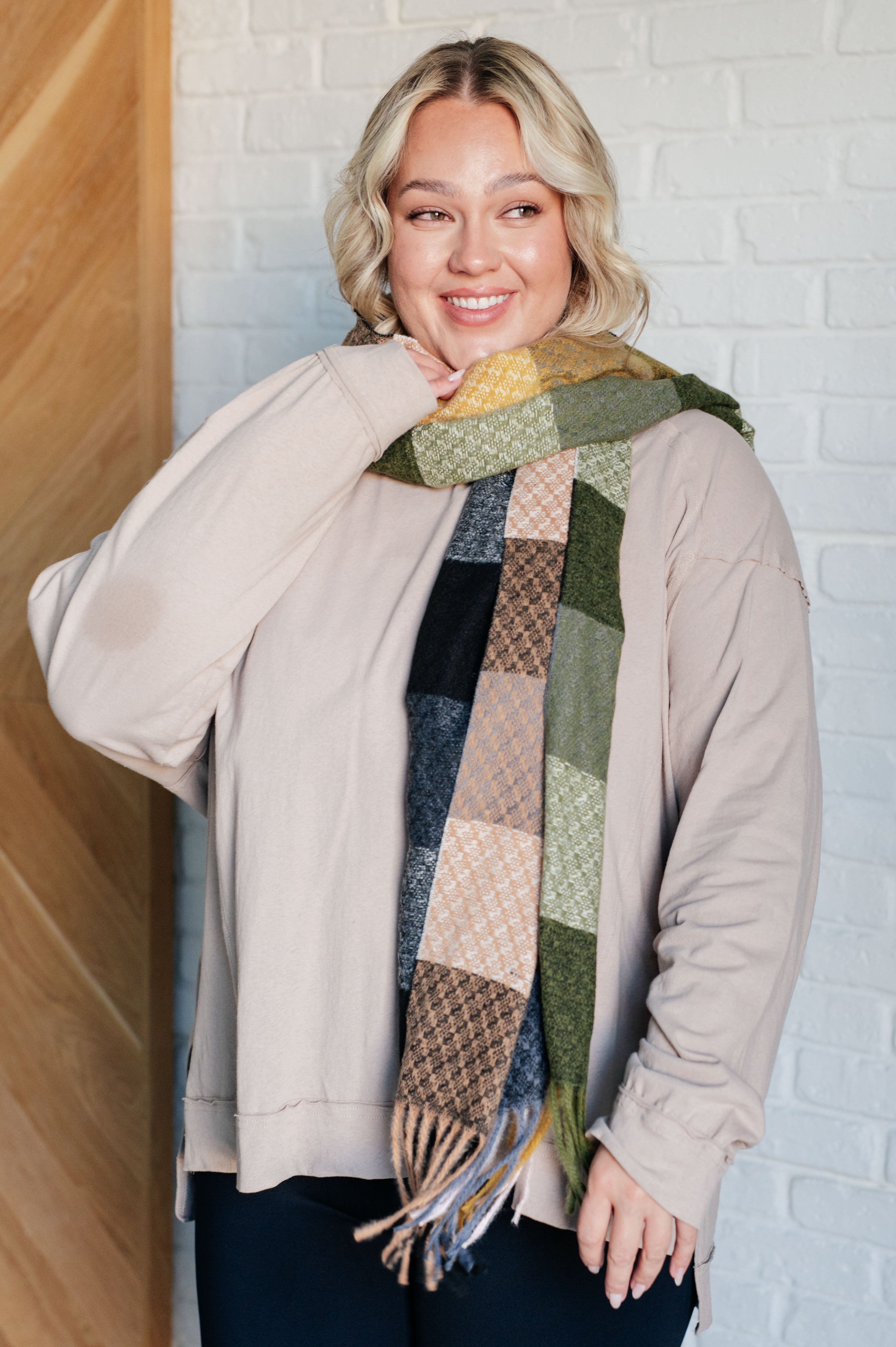 Smiling woman with blonde hair wearing a beige loose long sleeve top and a multi-colored checkered scarf indoors