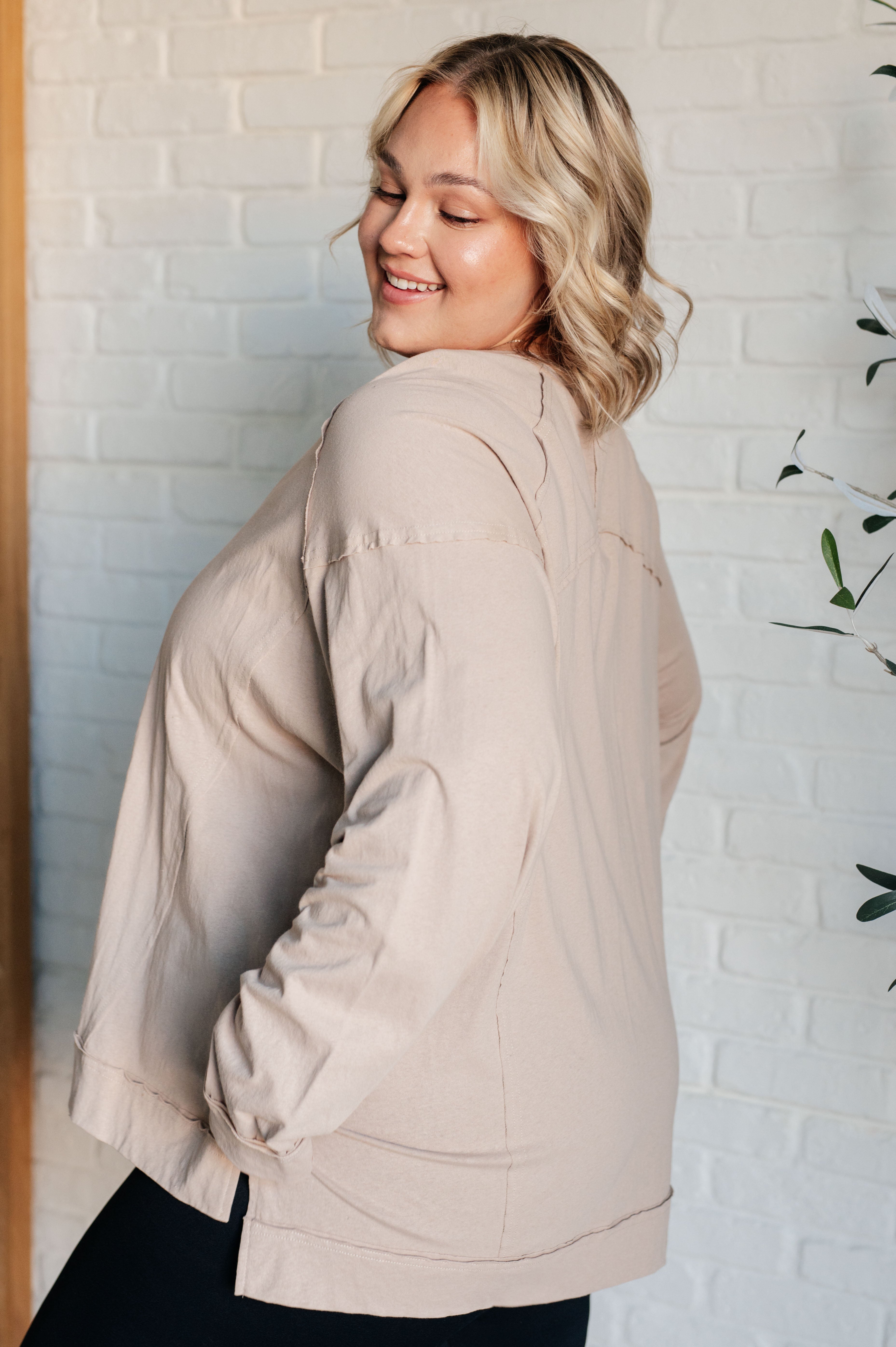 Smiling woman with short blonde hair wearing a beige long sleeve top with visible seam details indoors