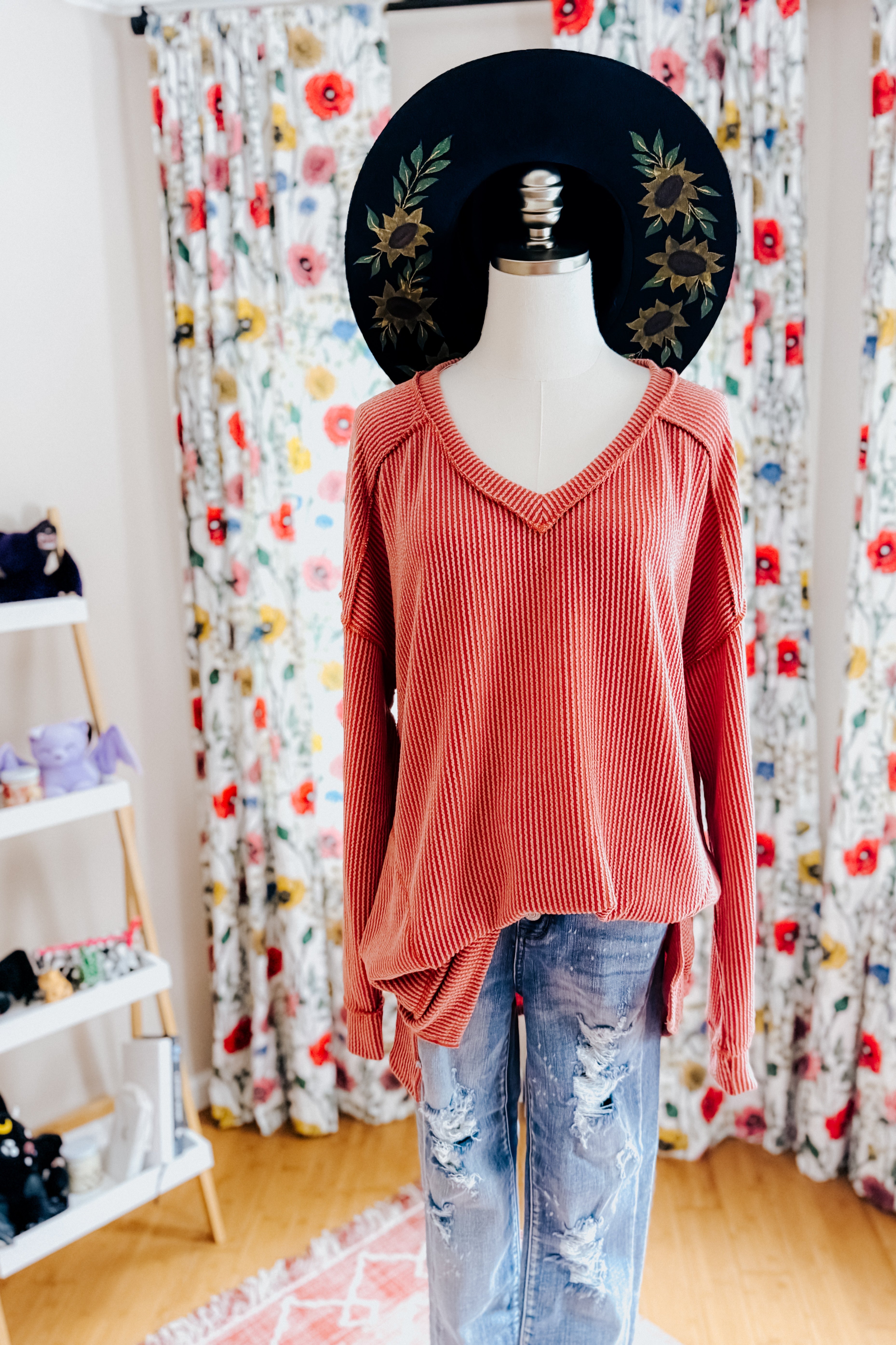 Mannequin dressed in rust ribbed long sleeve First and Foremost Rib Knit Top paired with distressed blue jeans and black wide brim hat with floral embroidery