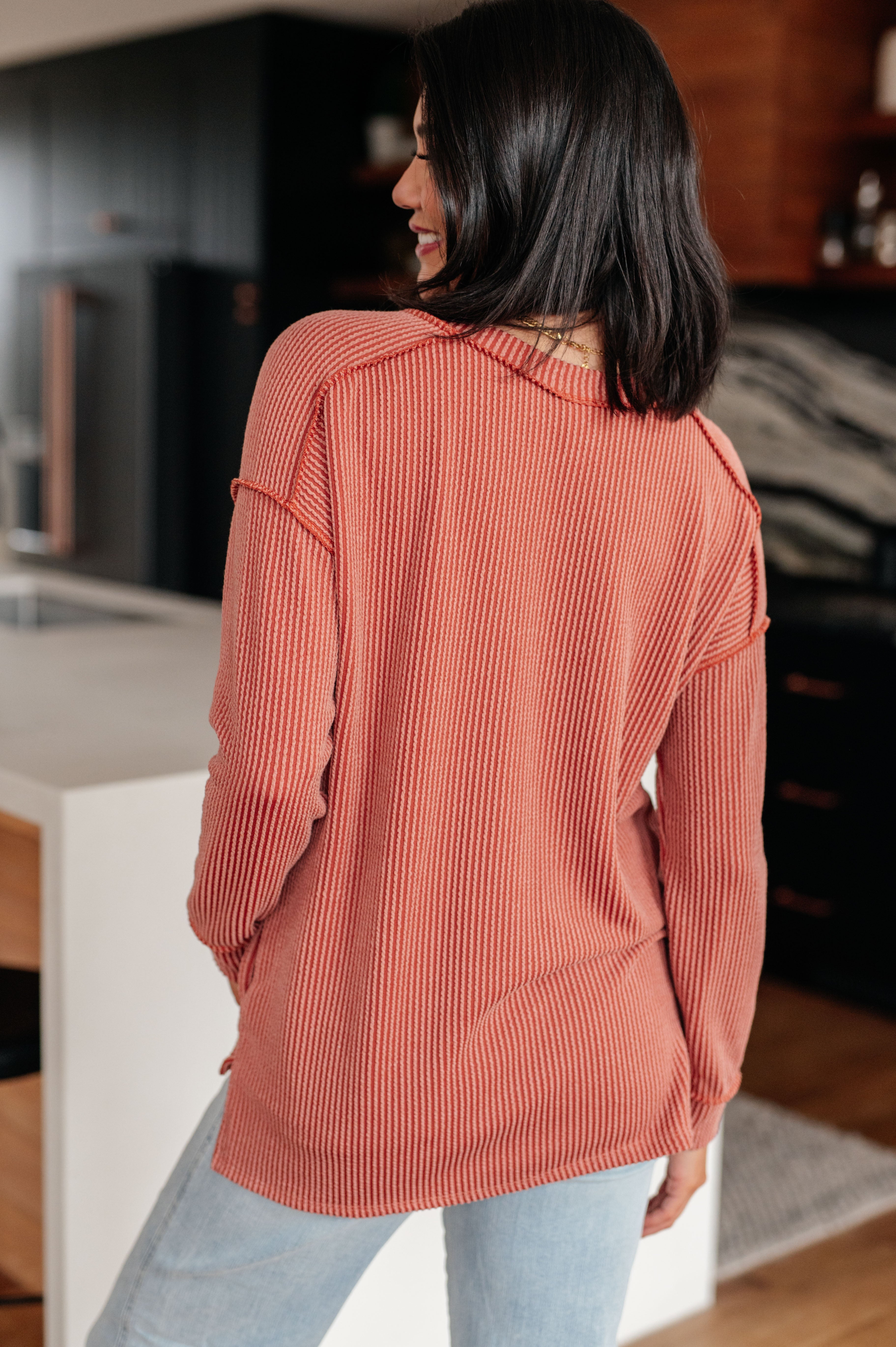 Woman seen from behind wearing rust colored First and Foremost Rib Knit Top with long sleeves standing in kitchen setting