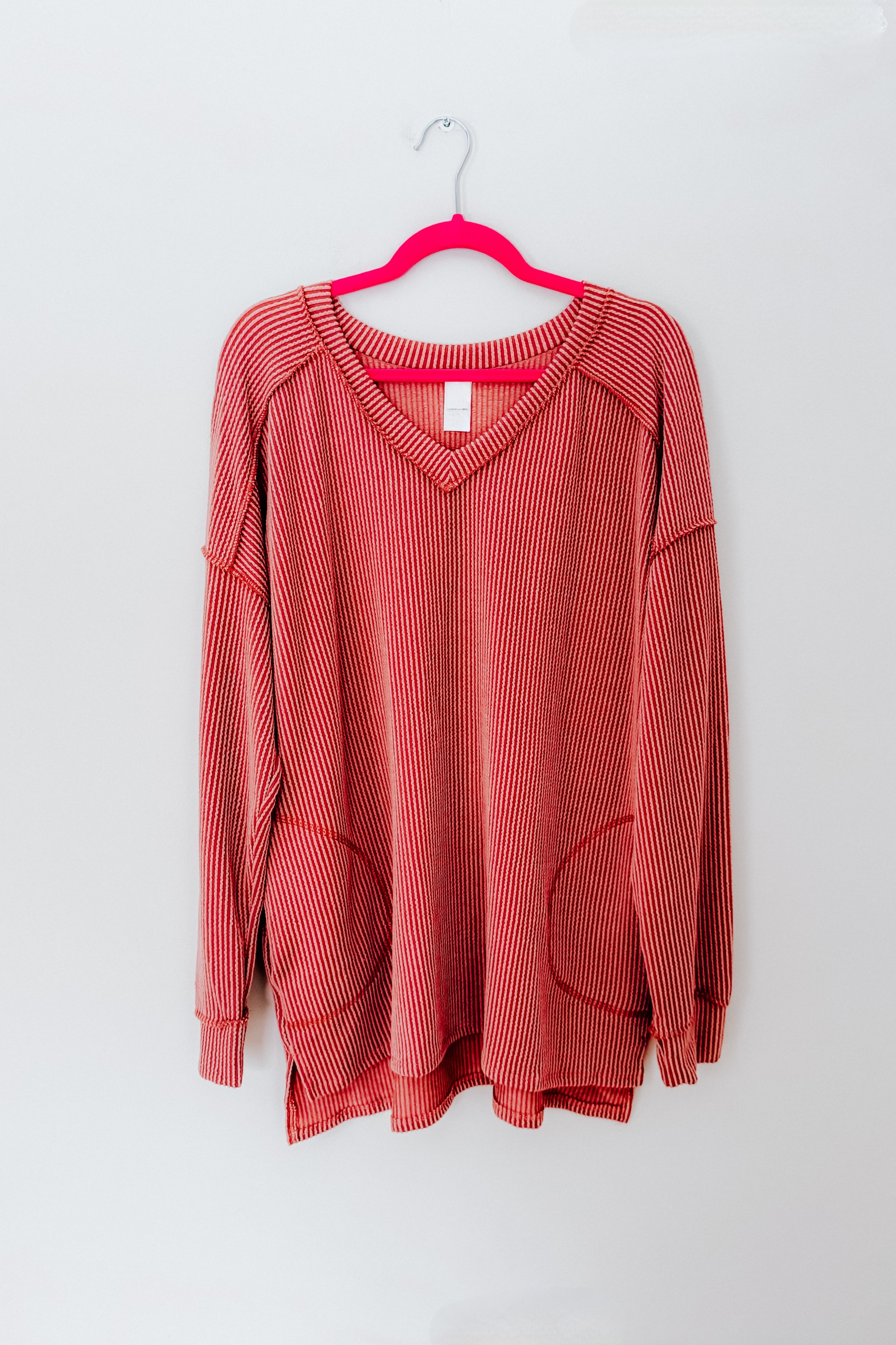 Rust striped long sleeve First and Foremost Rib Knit Top with V-neck and front pockets hanging on pink hanger against plain light background