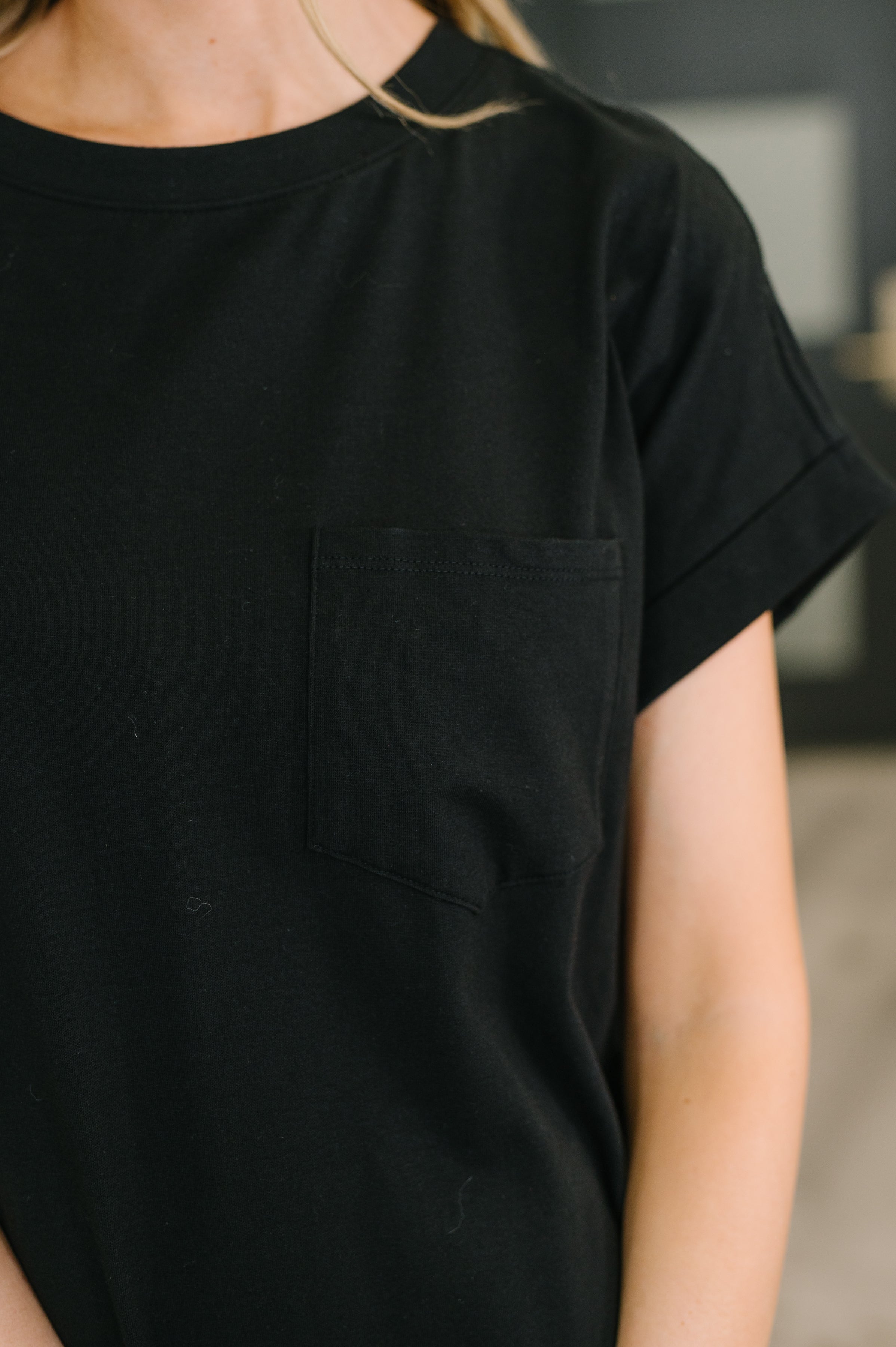 Close-up of black short-sleeve top featuring a round neckline and a chest pocket on the left side